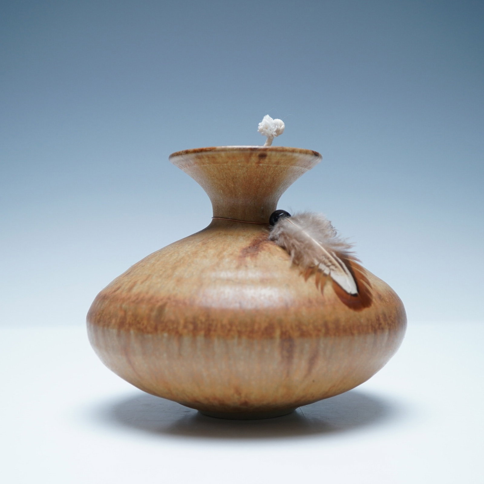 Signed Raku Pottery Spirit Vessel with Feather Accent: A beautifully crafted raku pottery spirit vessel featuring a smooth, earthy-toned glaze with natural variations in color and texture. The form is elegantly rounded with a flared rim, giving it a balan