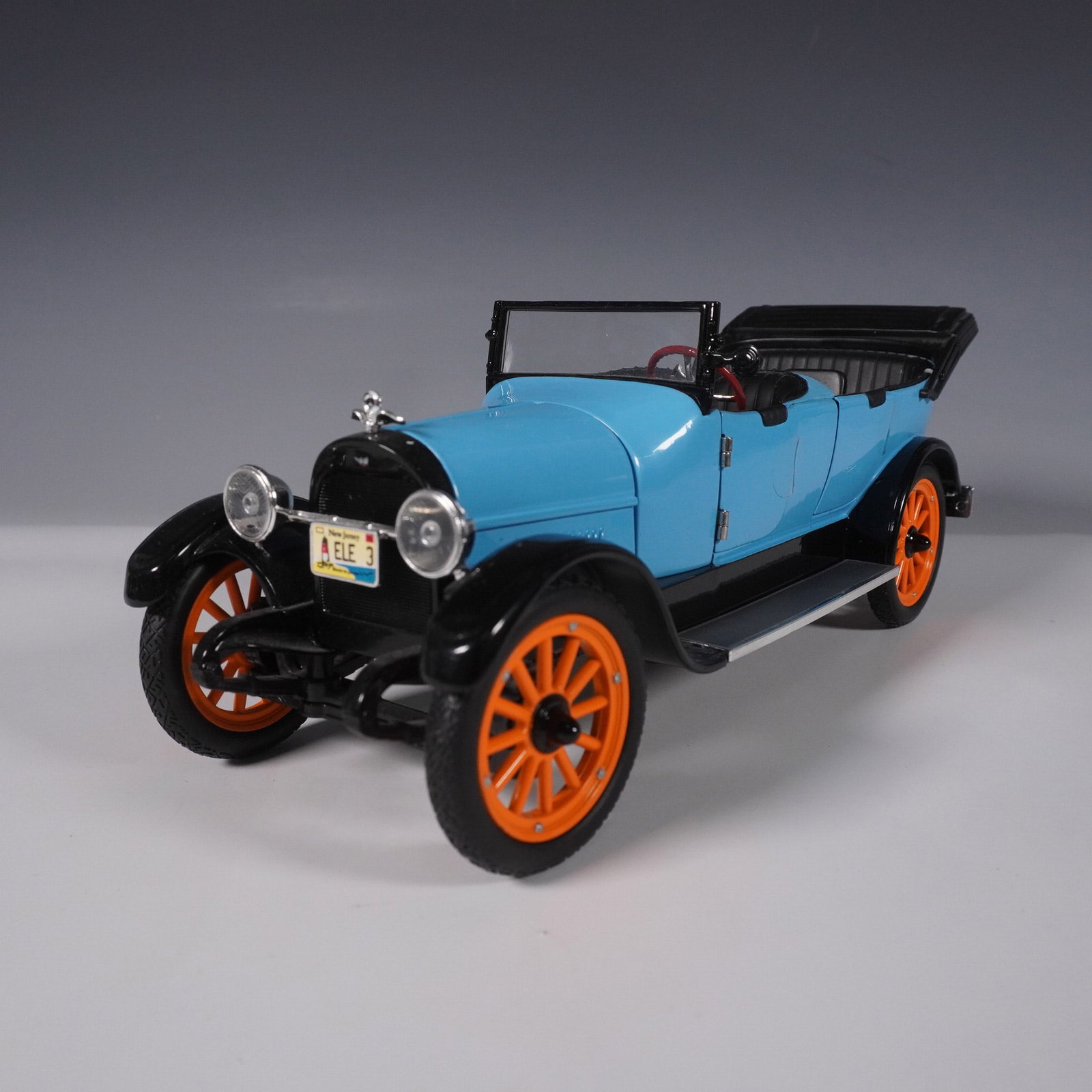 Diecast 1920s Touring Car Model, Blue with Orange Wheels: This highly detailed diecast model replicates a classic 1920s touring car with a striking blue body, black fenders, and vibrant orange-spoked wheels. The open-top design features a black folding roof,