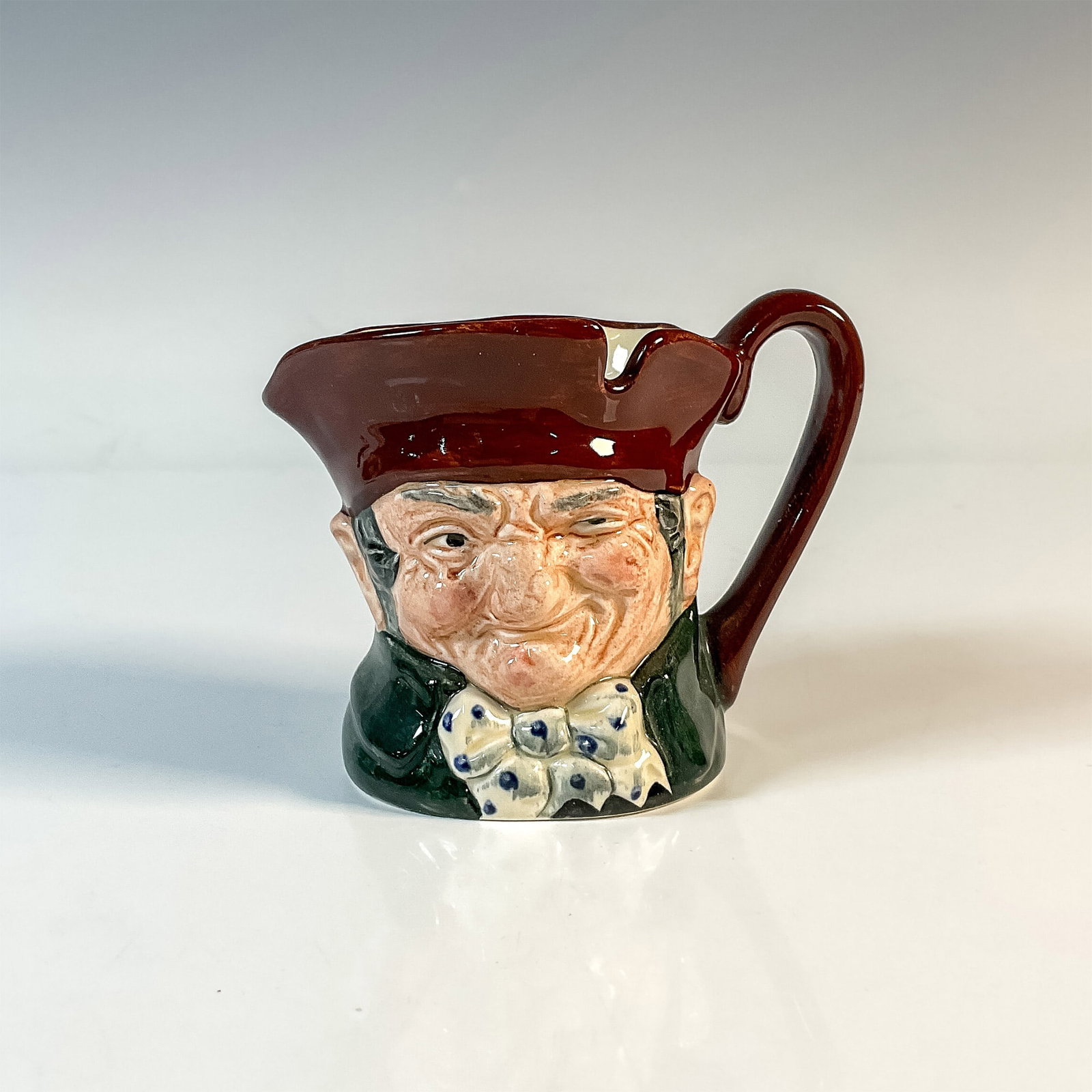 Old Charley D5527 - Small - Royal Doulton Character Jug: Brown hat; dark green coat; blue polka- dot bow tie. Royal Doulton backstamp. Artist: Charles J. Noke Issued: 1935 - 1983 Dimensions: 3.25"H Country of Origin: England