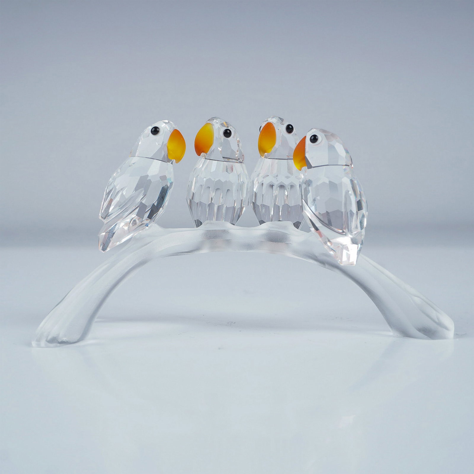 Swarovski Crystal Figurine, Baby Lovebirds: A charming Swarovski crystal figurine featuring four baby Lovebirds perched on a frosted three-pronged arch branch. Part of the Feathered Beauties theme, these faceted clear crystal Lovebirds showcase