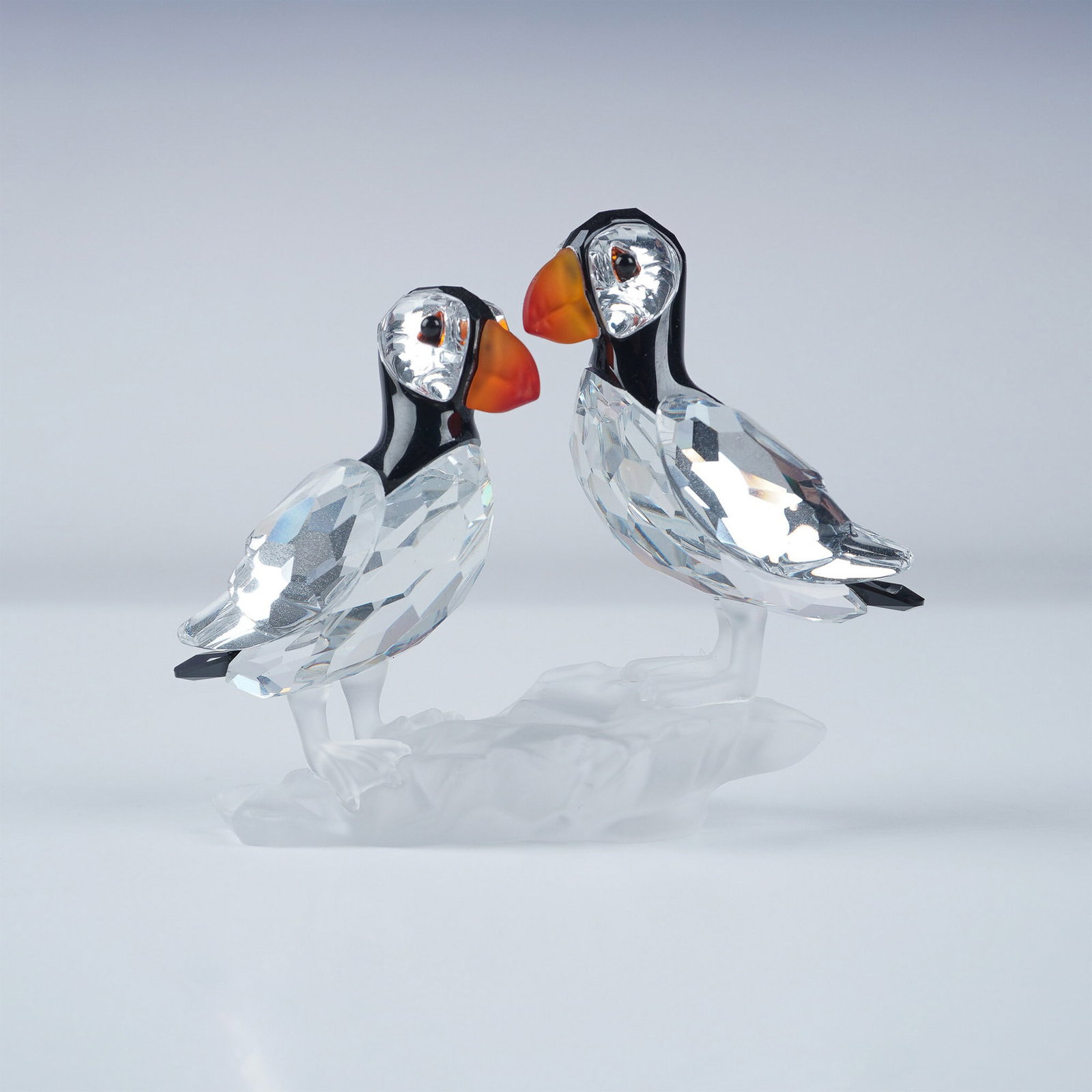 Swarovski Crystal Figurine, Puffins with Original Box: Part of the Feathered Beauties theme group, this Swarovski crystal figurine features a pair of puffins crafted in clear and jet crystal with mirror backing. Their striking fire opal beaks exhibit a ra