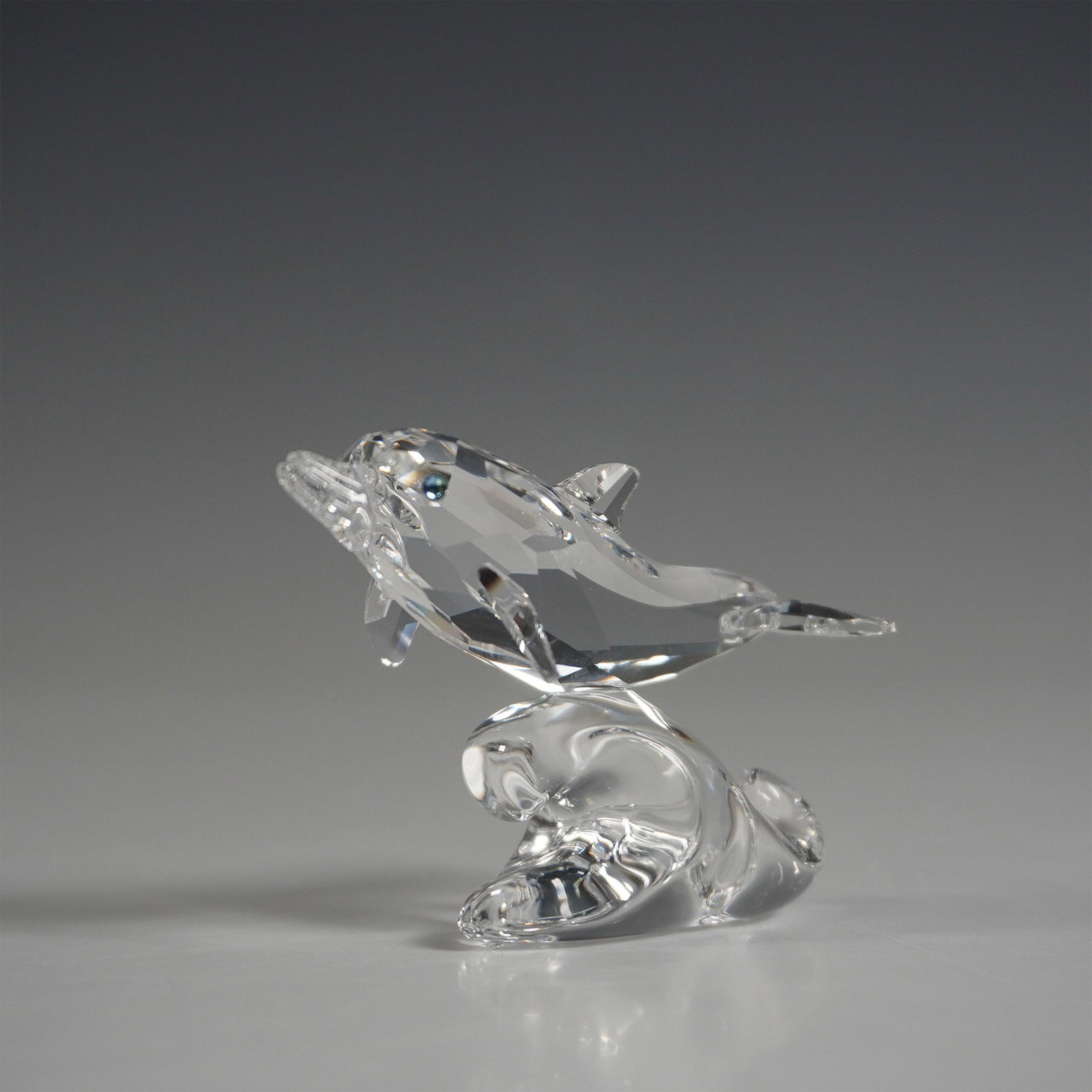 Swarovski Crystal Figurine, Baby Dolphin: A charming Swarovski crystal figurine featuring a baby dolphin, part of the Aquatic Worlds theme group. The dolphin is crafted in faceted clear crystal, with eyes in Wal crystal, gracefully leaping ov