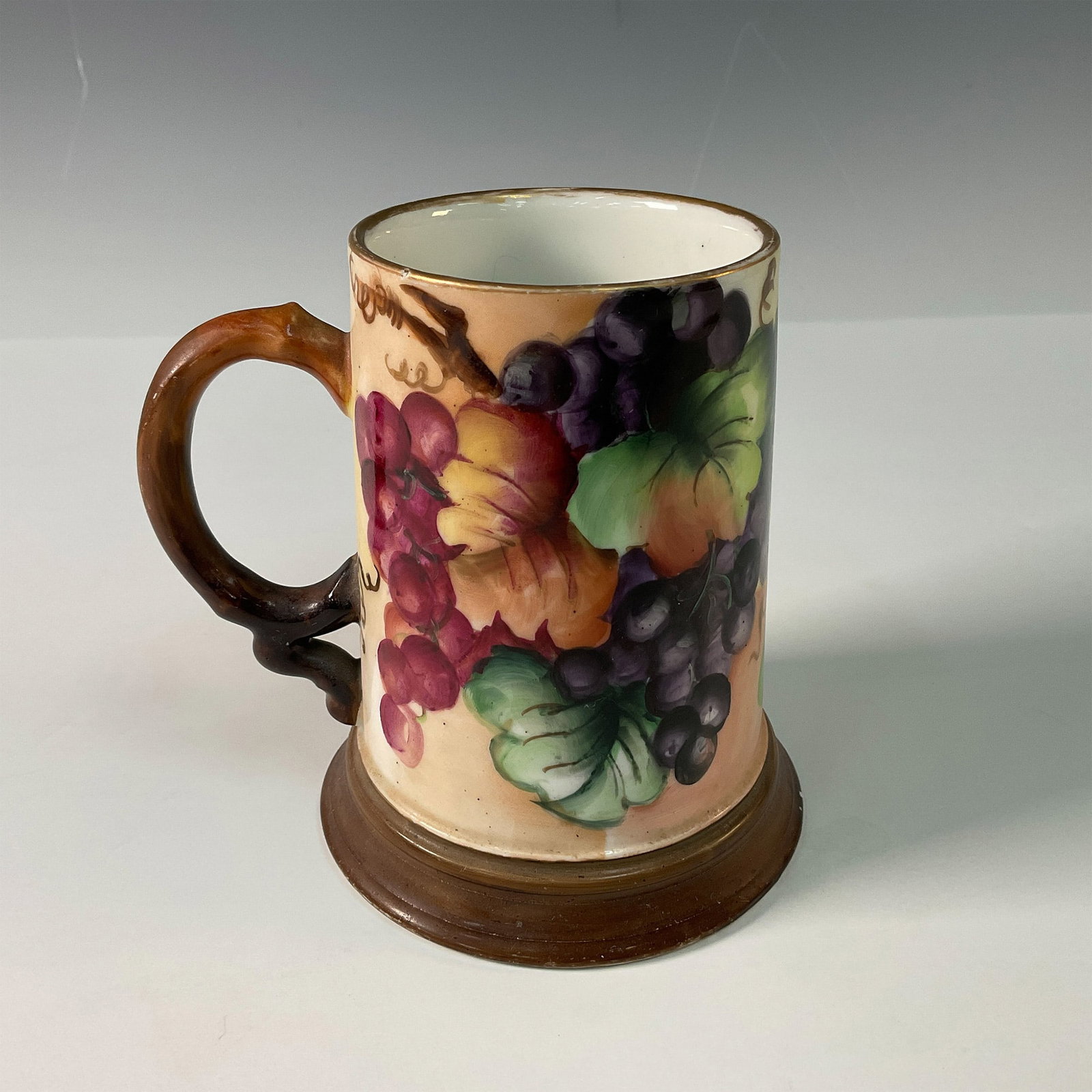 Jean Pouyat Limoges Grapevines Design Mug: A finely crafted porcelain mug from Limoges, France, featuring a vibrant hand painted design of colorful grapes and foliage. The mug is accented with a rustic brown handle, complementing its detailed 