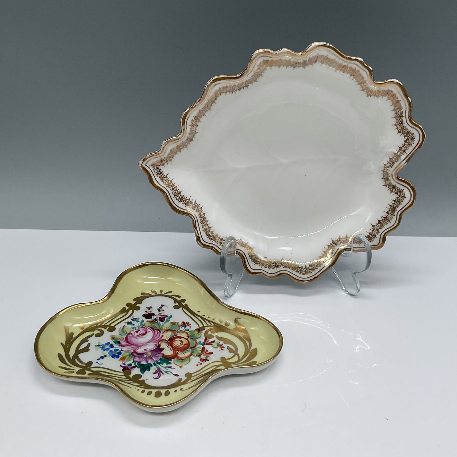 2pc Limoges France Porcelain Dresser Trays with Gilt Accents: A pair of Limoges France porcelain dresser trays with elegant gilded accents. The larger tray, 7"L x 6"W, features a scalloped edge with gold trim and a refined white glaze. The smaller tray showcases