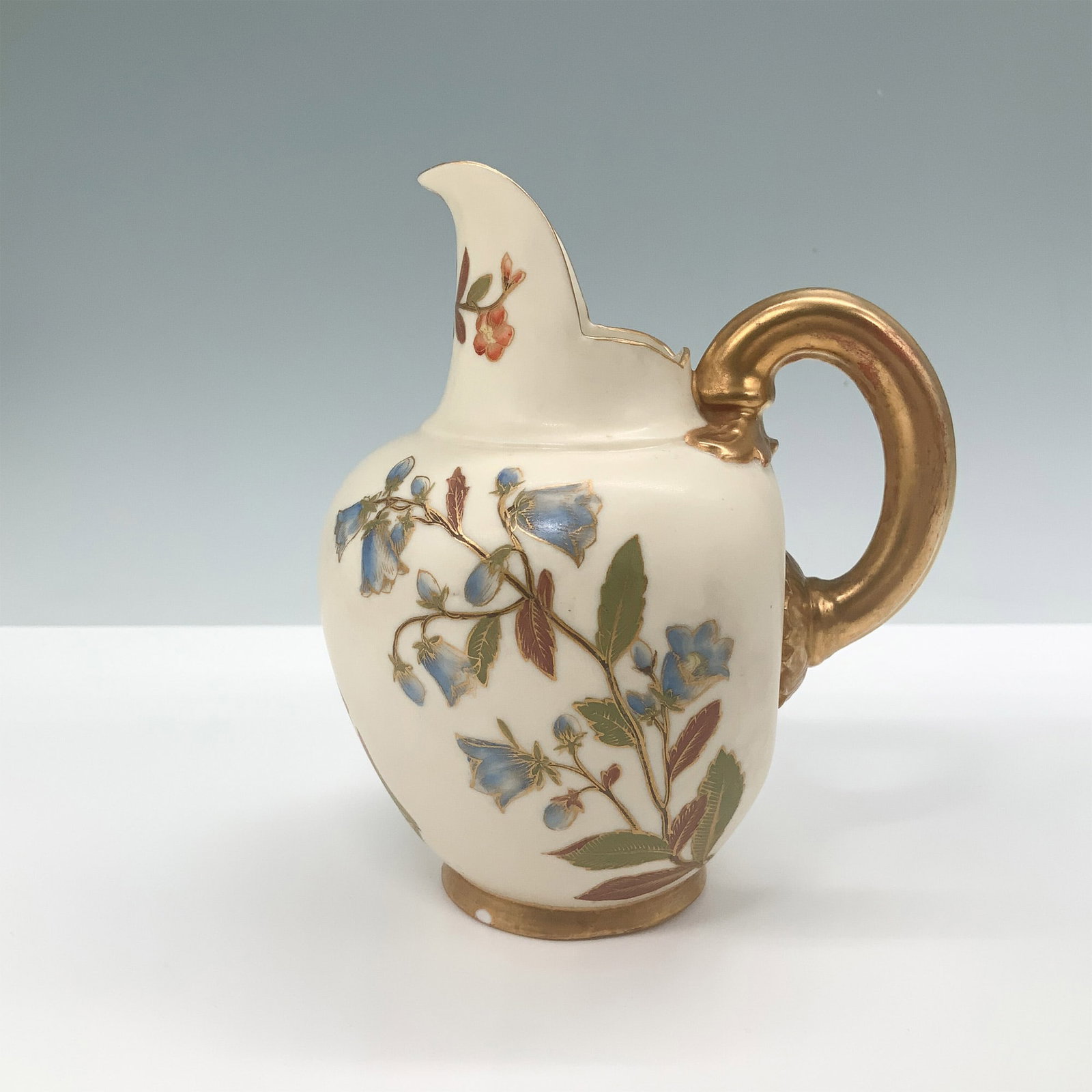 Royal Worcester Porcelain Hand Painted Floral Creamer: Royal Worcester porcelain creamer featuring an elegant hand-painted floral design with gold accents. The piece is adorned with intricate detailing, including a gilded handle and base. The bottom bears