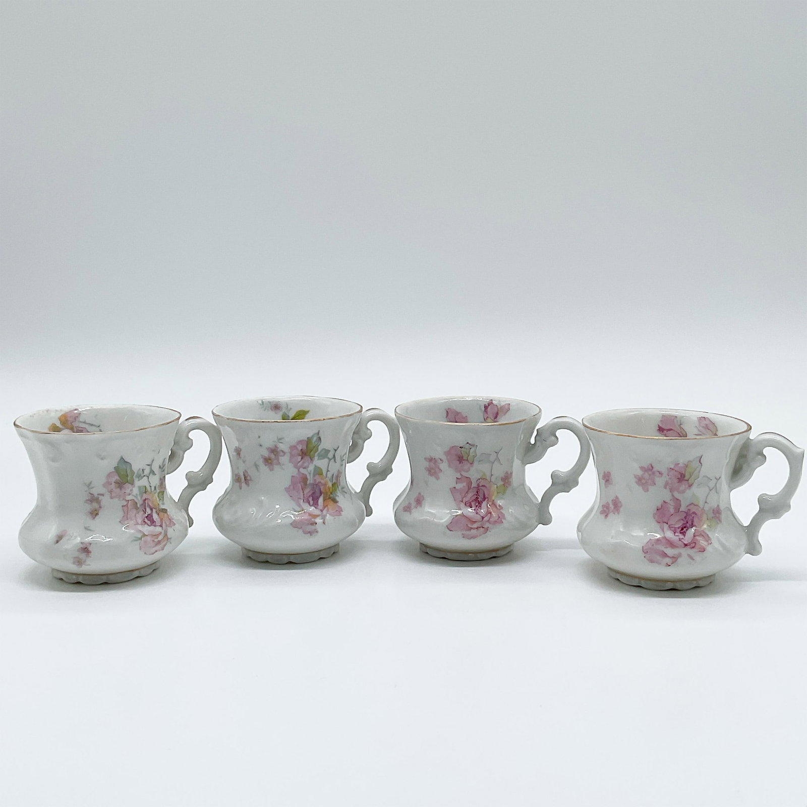 Set of Four LS&S Carlsbad Austria Porcelain Miniature Cups: Set of four porcelain miniature cups marked "LS&S Carlsbad Austria." Each features floral patterns in pink and yellow with ornate handles, scalloped bases, and gilded rims. Measuring 2 inches tall, th