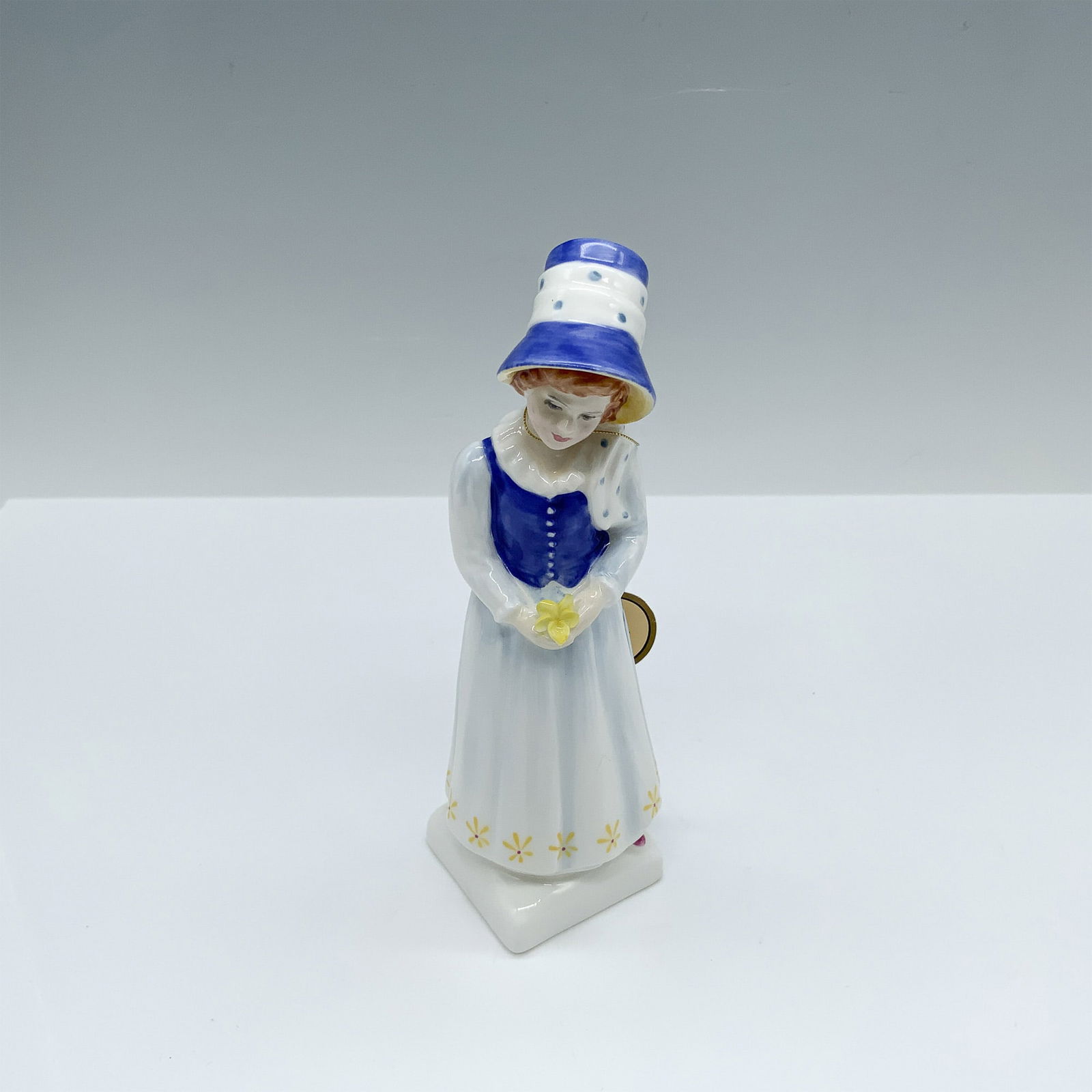 Lucy - HN2863 - Royal Doulton Figurine: This girl in a blue and white dress with a matching bonnet figure from the Kate Greenaway Collection is based of one of Kate's books named Under The Window which contains idyllic verses concerning chi