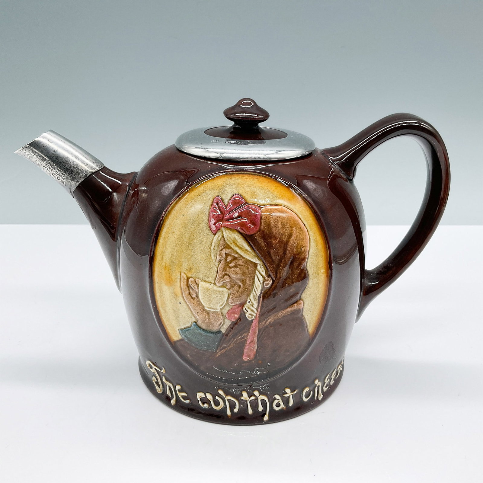 Royal Doulton Kingsware The Cup That Cheers Teapot Sterling: Royal Doulton Kingsware teapot featuring The Cup That Cheers motif, showcasing a relief portrait of a woman enjoying tea. This exquisite piece is finished in the signature glossy brown glaze character