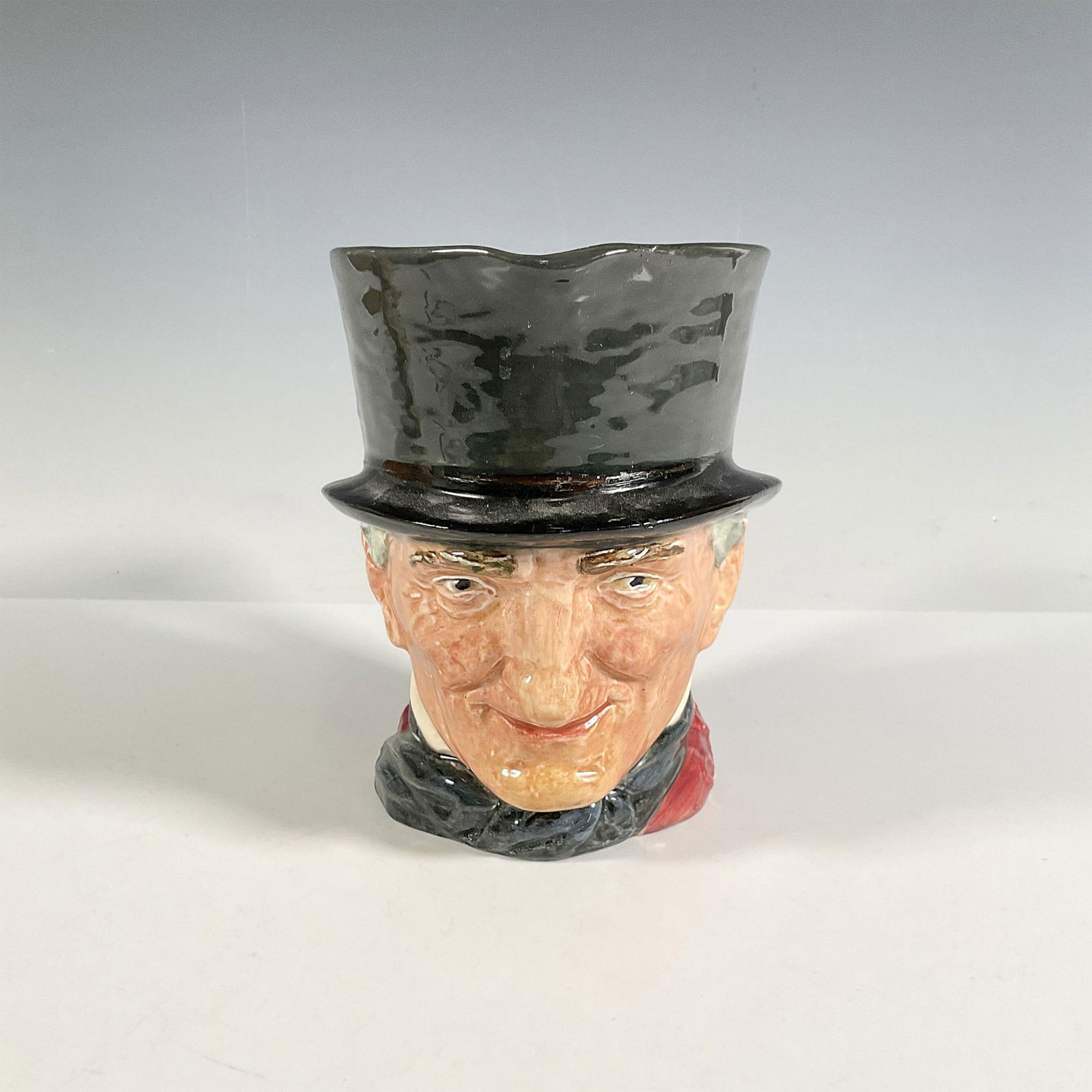 Royal Doulton Large Character Jug, John Peel D5612: Hand painted figural jug with the handle shaped as a grey, brown, black and white riding crop. Dark grey hat, maroon coat with dark blue bow tie. Royal Doulton backstamp. Artist: Harry Fenton Issued: