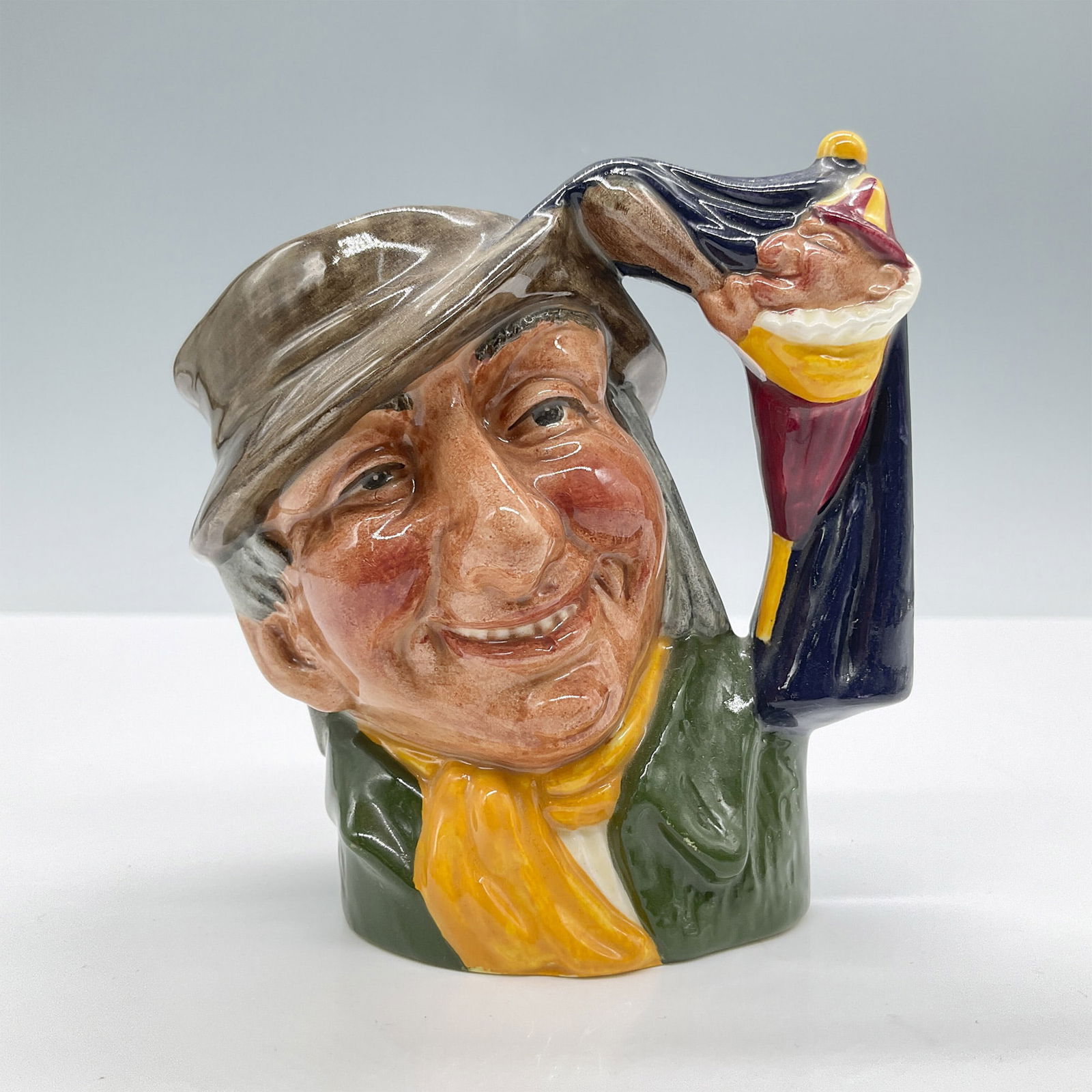 Punch and Judy Man D6593 Small Royal Doulton Character Jug: Brown hat; green coat; yellow scarf. Royal Doulton backstamp. Artist: David B. Biggs Issued: 1964 - 1969 Dimensions: 3.25''L x 2.75''W x 4.25''H Country of Origin: England