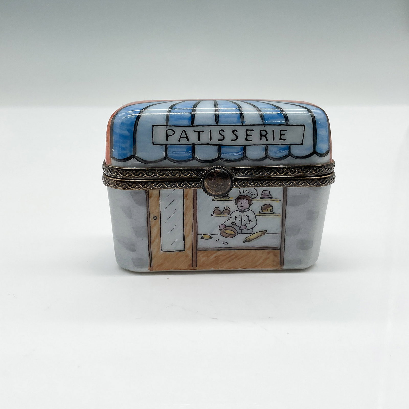 Limoges Hand-Painted Porcelain Patisserie Trinket Box: A charming Limoges hand-painted porcelain trinket box, shaped like a French patisserie storefront. This intricately detailed box features a blue and white striped awning, a bakery window with a chef p