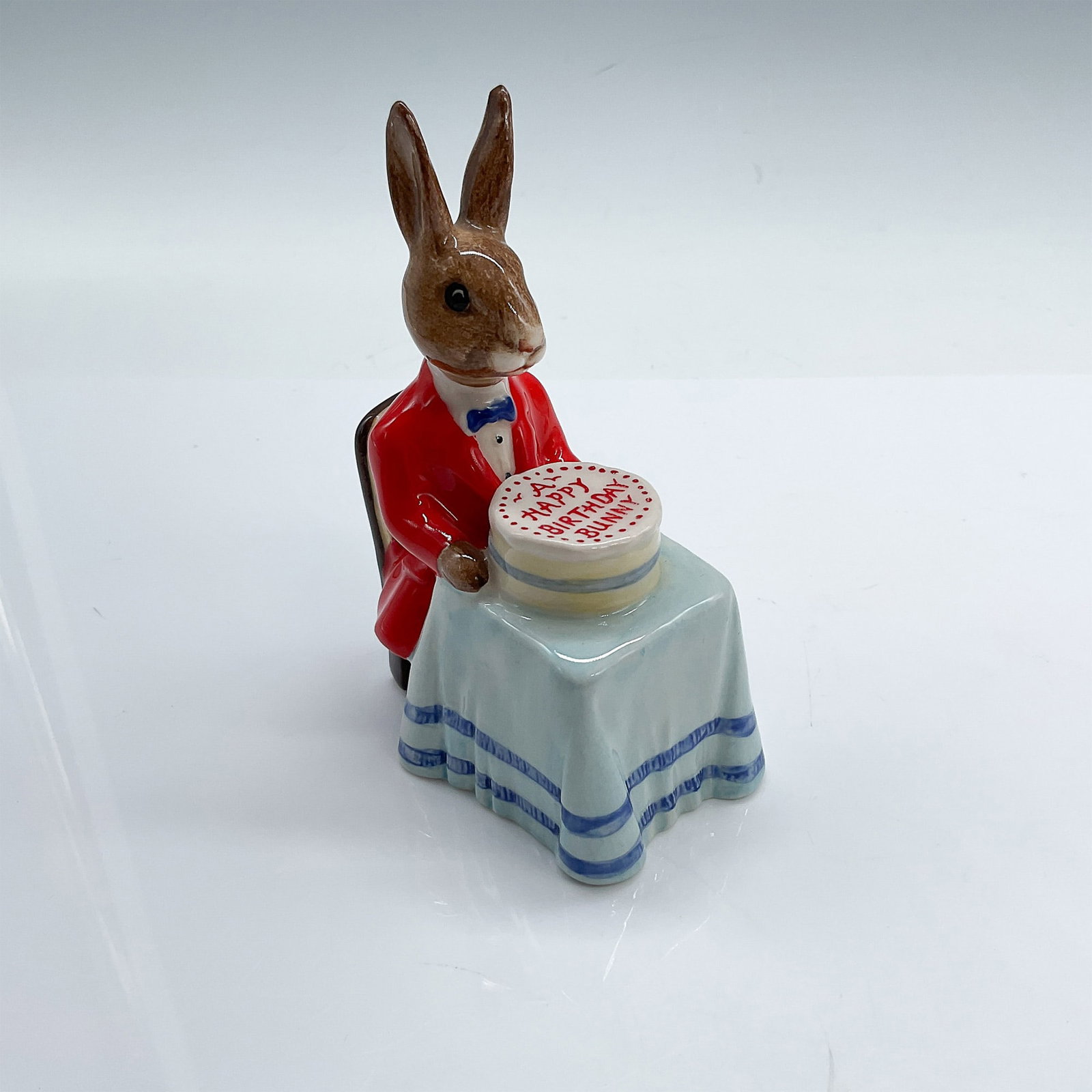 Royal Doulton Bunnykins Figurine, Happy Birthday DB21: Royal Doulton Bunnykins figurine titled "Happy Birthday Bunnykins," model DB21, featuring a bunny wearing a red jacket with a bow tie and seated at a table with a cake inscribed "Happy Birthday Bunny.