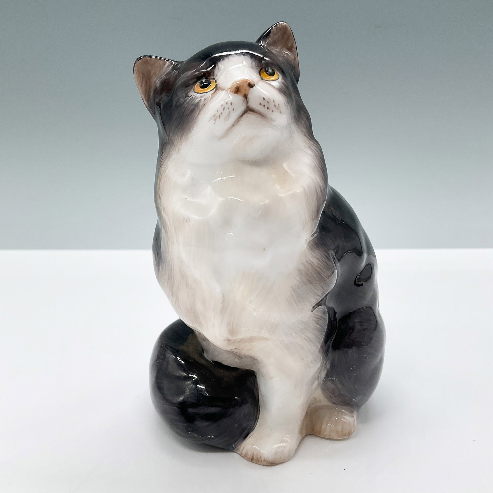 Royal Doulton Figurine, Black and White Cat HN999: This charming Royal Doulton figurine features a black and white cat seated in an attentive pose, capturing lifelike detail and personality. Designed in fine bone china, it measures 5"H and showcases t