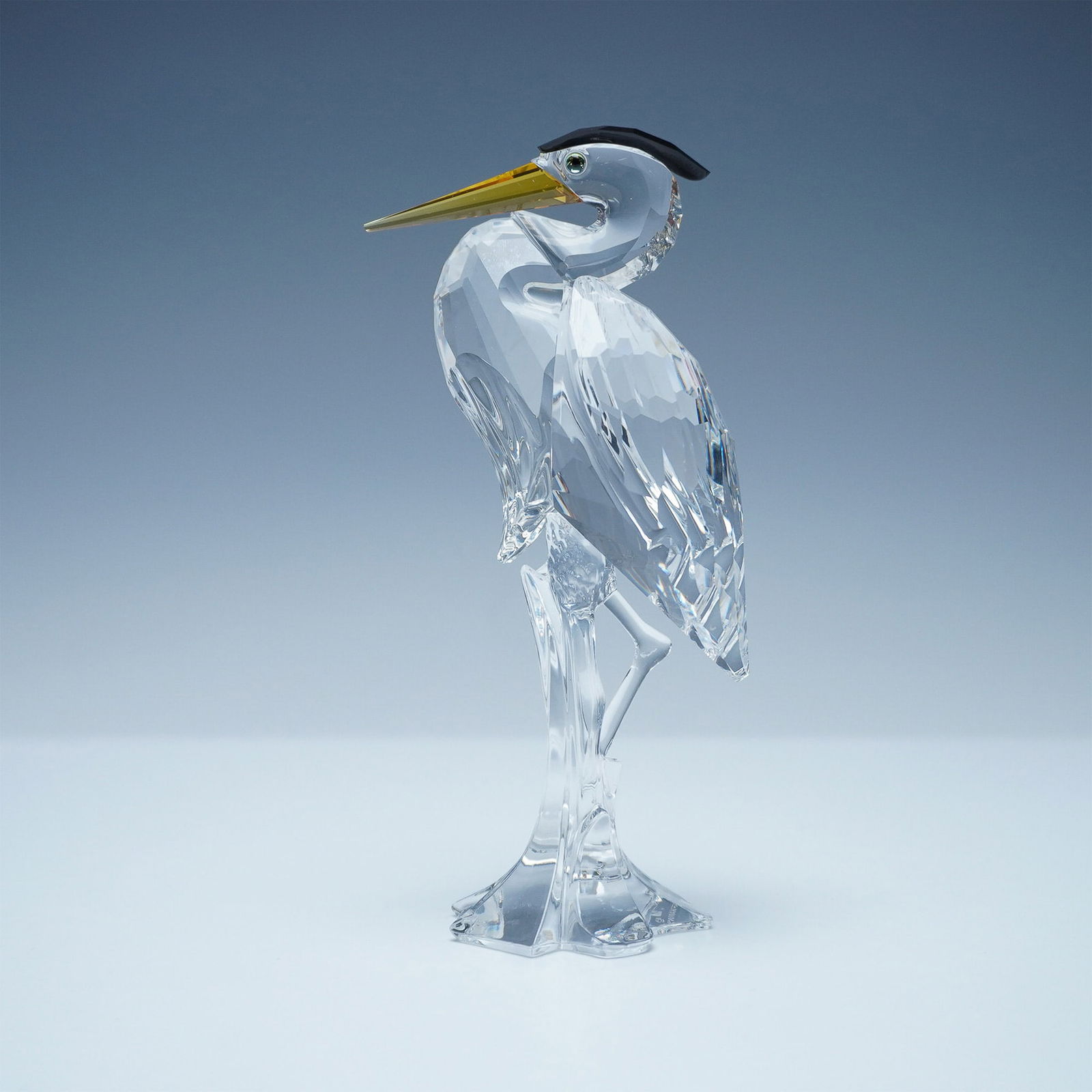 Swarovski Crystal Heron Figurine: This elegant Swarovski crystal heron figurine is a stunning representation of the majestic wading bird, crafted in clear faceted crystal with intricate detailing. The figurine features a golden beak,