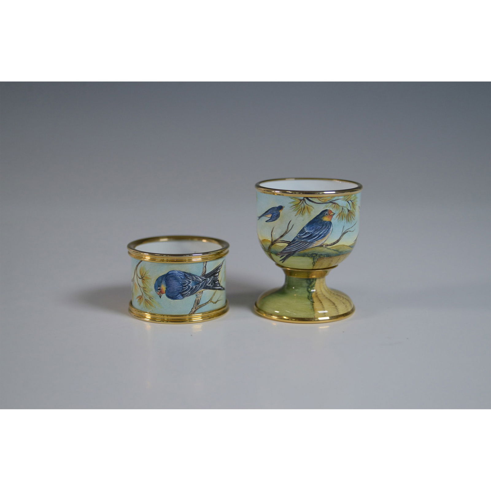 2pc Moorcroft Porcelain Egg Cup and Napkin Ring, Swallow Design: Moorcroft porcelain egg cup and napkin ring set featuring hand-painted swallows on a soft blue background with gold trim. Marked Moorcroft, Made in England, with handwritten trial piece notation dated