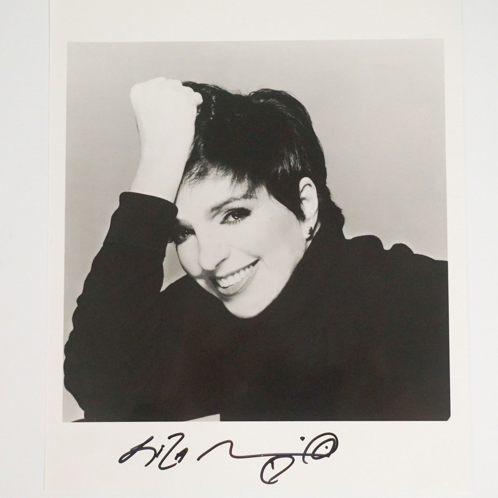 Liza Minnelli Signed Photograph with Certificate of Authenticity: A striking black and white photograph of Liza Minnelli, signed boldly in black ink. This glamorous portrait captures Minnelli in a classic pose, showcasing her signature short hair and radiant smile.
