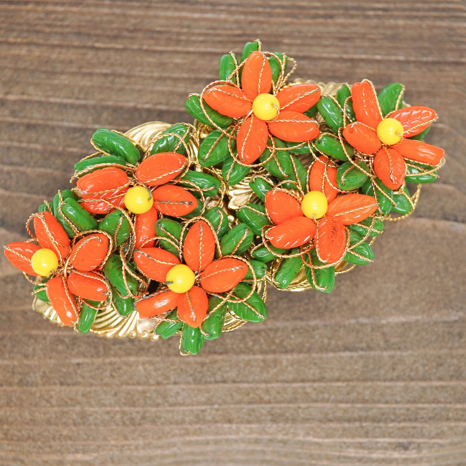 Christian Dior Gold Tone Floral Beaded Belt Buckle: This 2-piece belt buckle showcases an intricate floral design with vibrant orange and green glass beads, meticulously wired into a gold-tone filigree setting. The symmetrical composition features six-