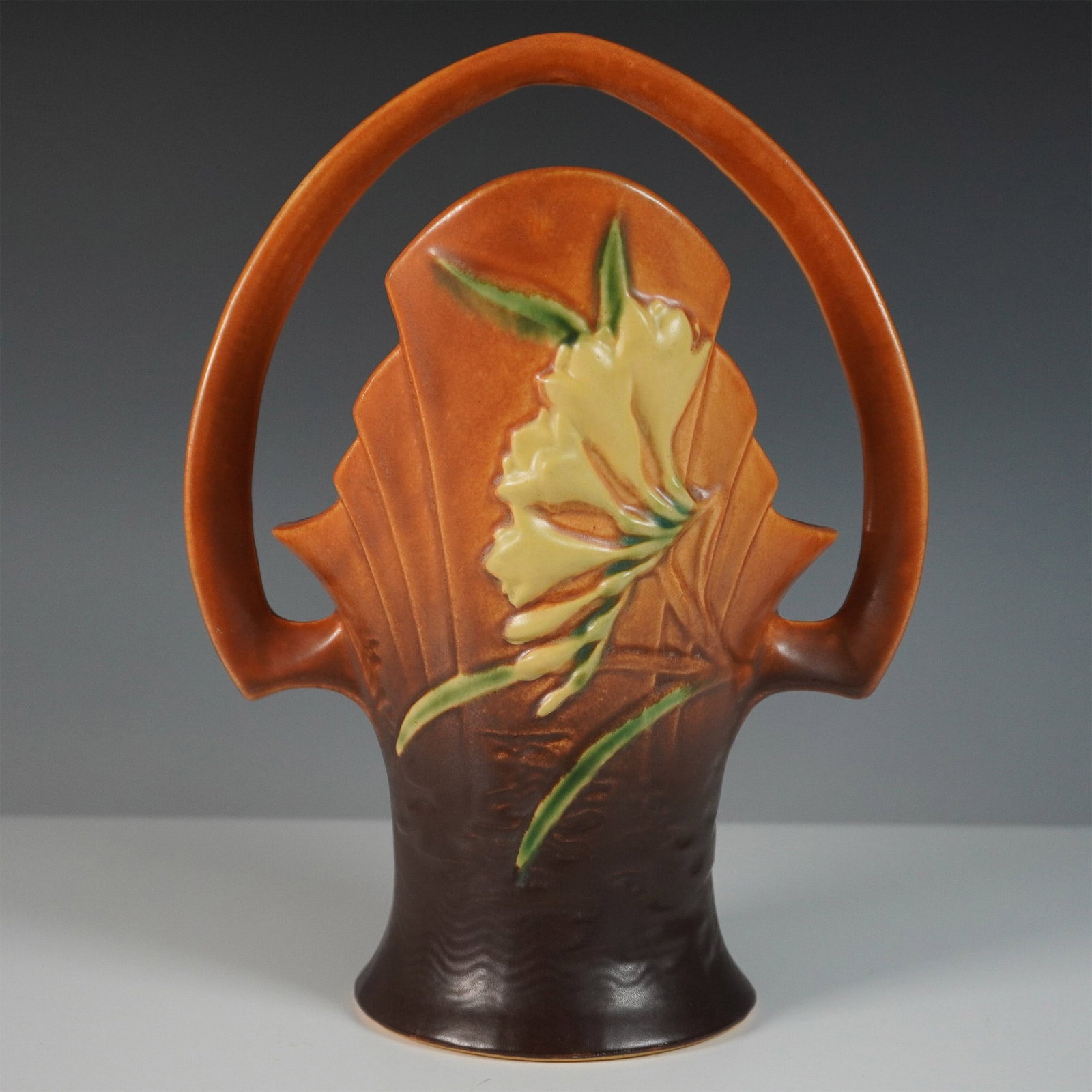 Roseville Pottery Ceramic Basket, Freesia: This Roseville Pottery Freesia basket is a striking example of the company?s signature Art Deco-influenced floral designs. Crafted in the vibrant tangerine glaze, this basket features embossed freesia