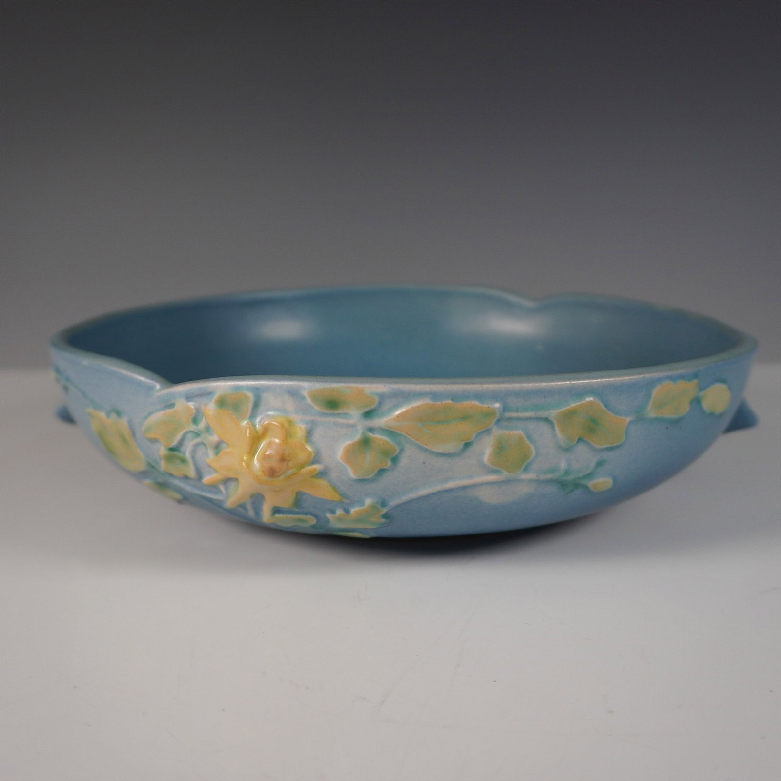 Roseville Blue Columbine Bowl: This piece is a classic example of the renowned Roseville Pottery craftsmanship from the mid-20th century. Featuring a raised floral motif of yellow columbine flowers with green leaves against a soft 