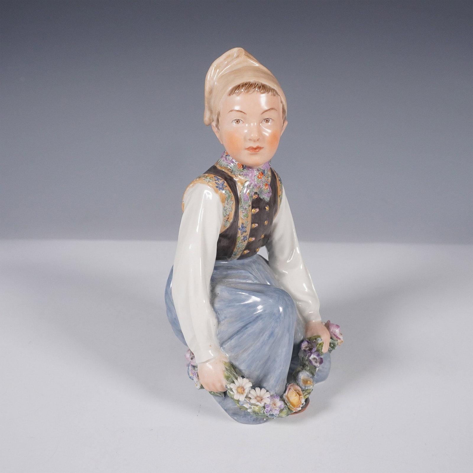 Royal Copenhagen Porcelain Figurine, Amager Girl: A finely crafted Royal Copenhagen porcelain figurine, model number 12414, depicting an Amager girl in traditional Danish attire. She is adorned in a delicate floral vest with intricate hand-painted de