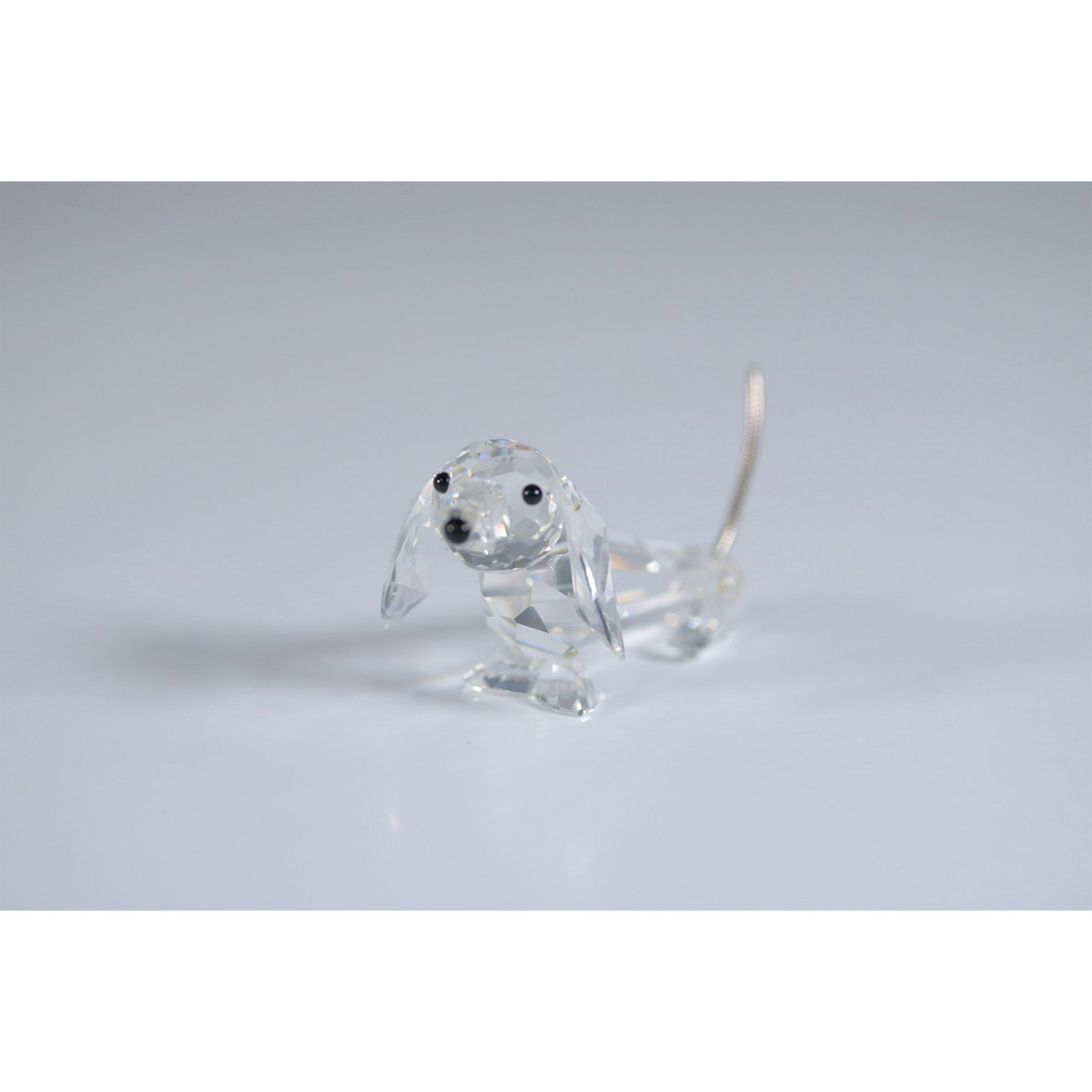 Swarovski Crystal Figurine, Dachshund: This retired Swarovski crystal figurine features a faceted clear crystal body, black eyes, a black nose, and coil metal tail. An endearing and highly collectible representation of the beloved breed, t