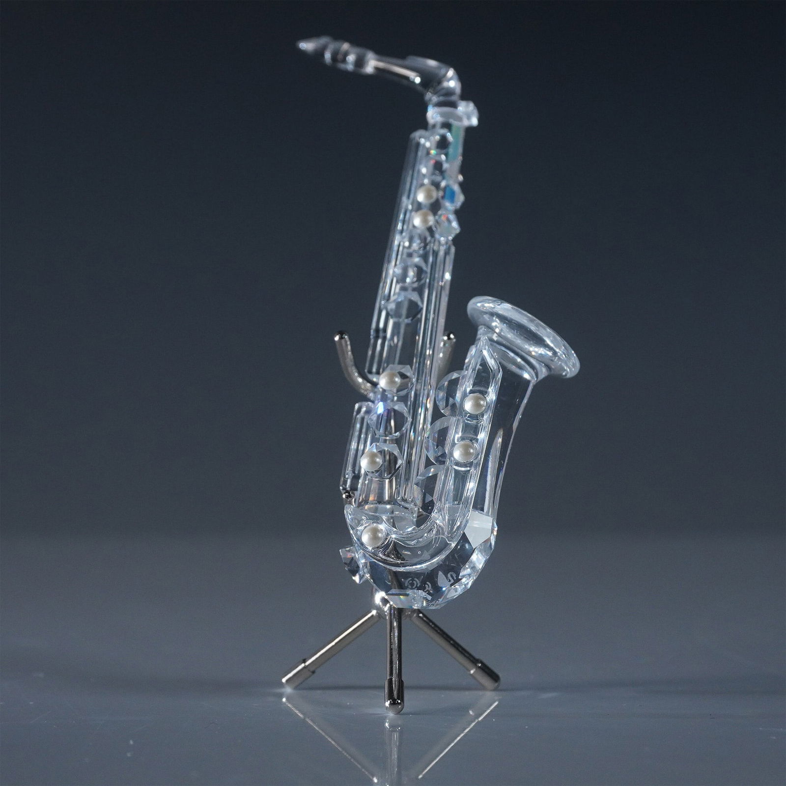 Swarovski Crystal Figurine, Saxophone with Stand: A stunning Swarovski Silver Crystal saxophone figurine, designed with intricate detailing, featuring a faceted crystal body accented with frosted and clear crystal elements. The saxophone is mounted o