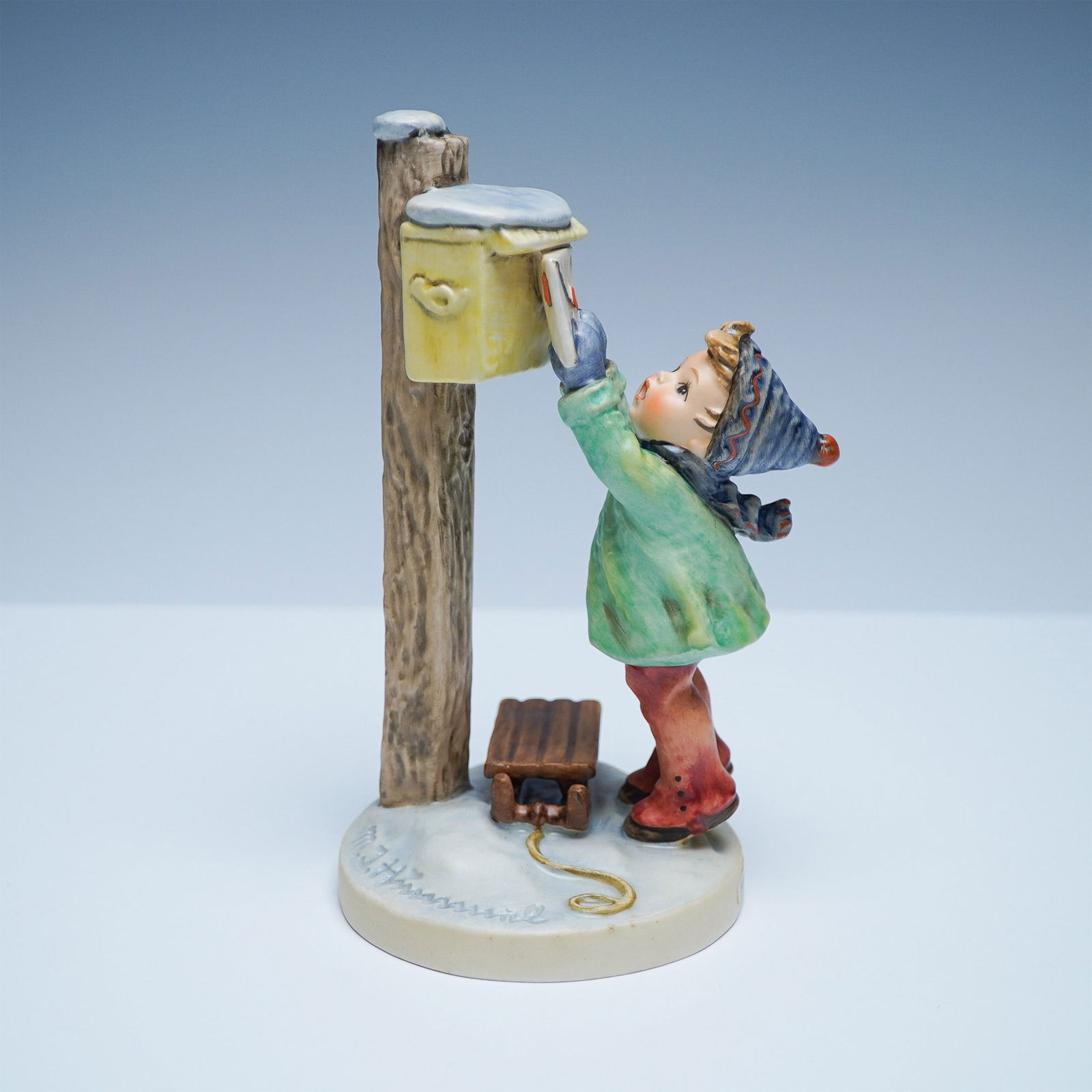 Goebel Hummel Porcelain Figurine, A Letter to Santa Claus: Charming Goebel Hummel figurine depicting a young child in a winter outfit reaching up to mail a letter to Santa. Hand-painted in soft hues, it features a textured wooden post-mounted mailbox, a snow-