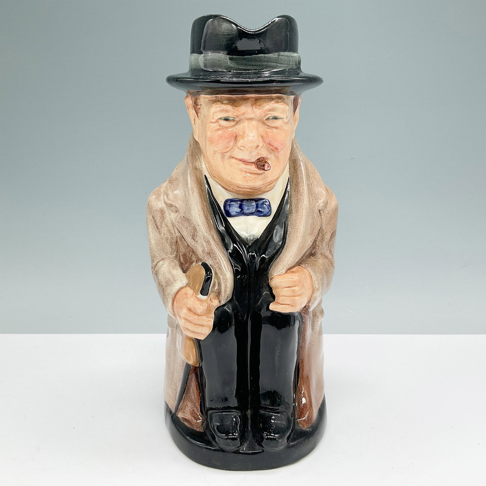 Royal Doulton Toby Jug, Winston Churchill: Royal Doulton Toby Jug depicting Winston Churchill, featuring the iconic British Prime Minister in a brown coat and black hat, with a cigar in hand. Stamped on the underside with the Royal Doulton bac
