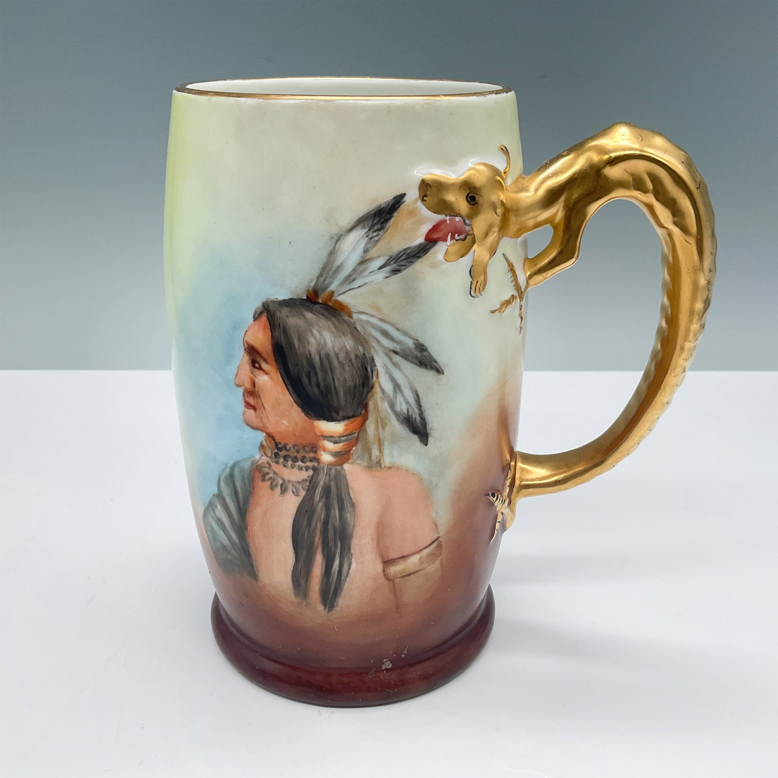 J.P.L. Limoges Tankard Mug, Native American Portrait: A J.P.L. (Jean Pouyat Limoges) France tankard mug featuring a hand-painted depiction of a Native American profile, highlighted with vibrant colors and detailed gold accents. The handle is sculpted in 