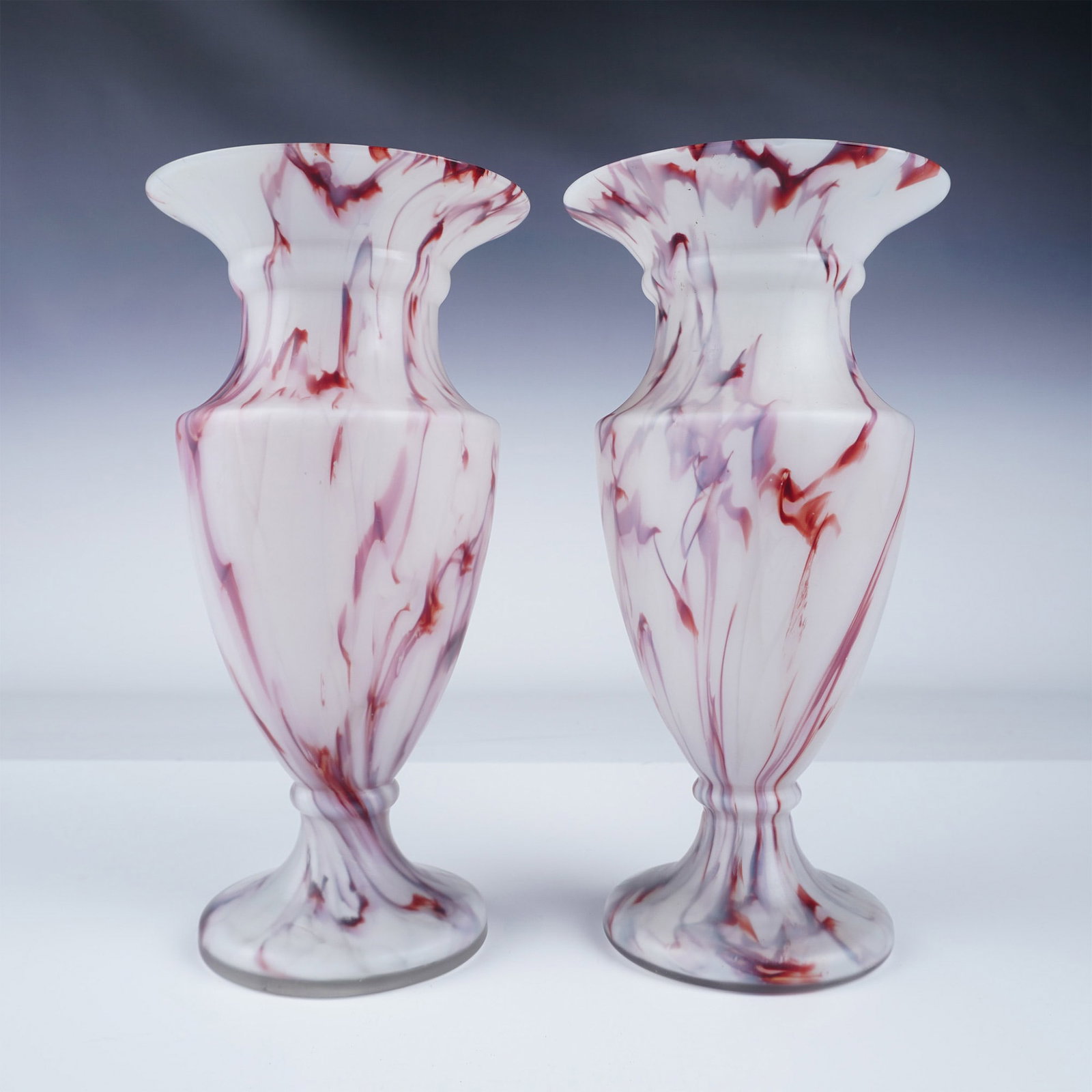2pc Frosted Glass Trophy Vases, Red Veining: Pair of frosted glass trophy-shaped vases measuring 10"H. The vases feature a milky white body with striking red veining throughout the glass, complemented by a matte finish. Unmarked, these decorativ