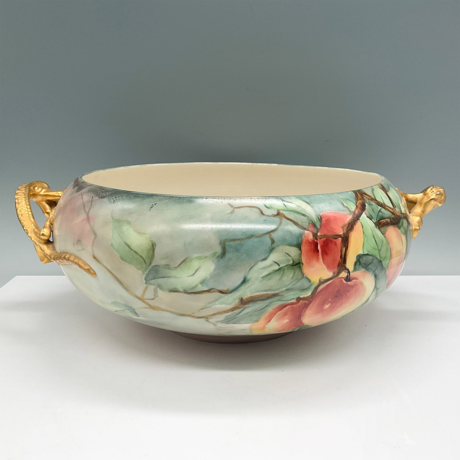 Vintage Dragon Handle Bowl with Peaches Design: Hand-painted vintage bowl featuring a vibrant peaches design with delicate foliage. The piece is adorned with intricate gilded dragon handles, adding a touch of elegance. The base is marked with "Aust