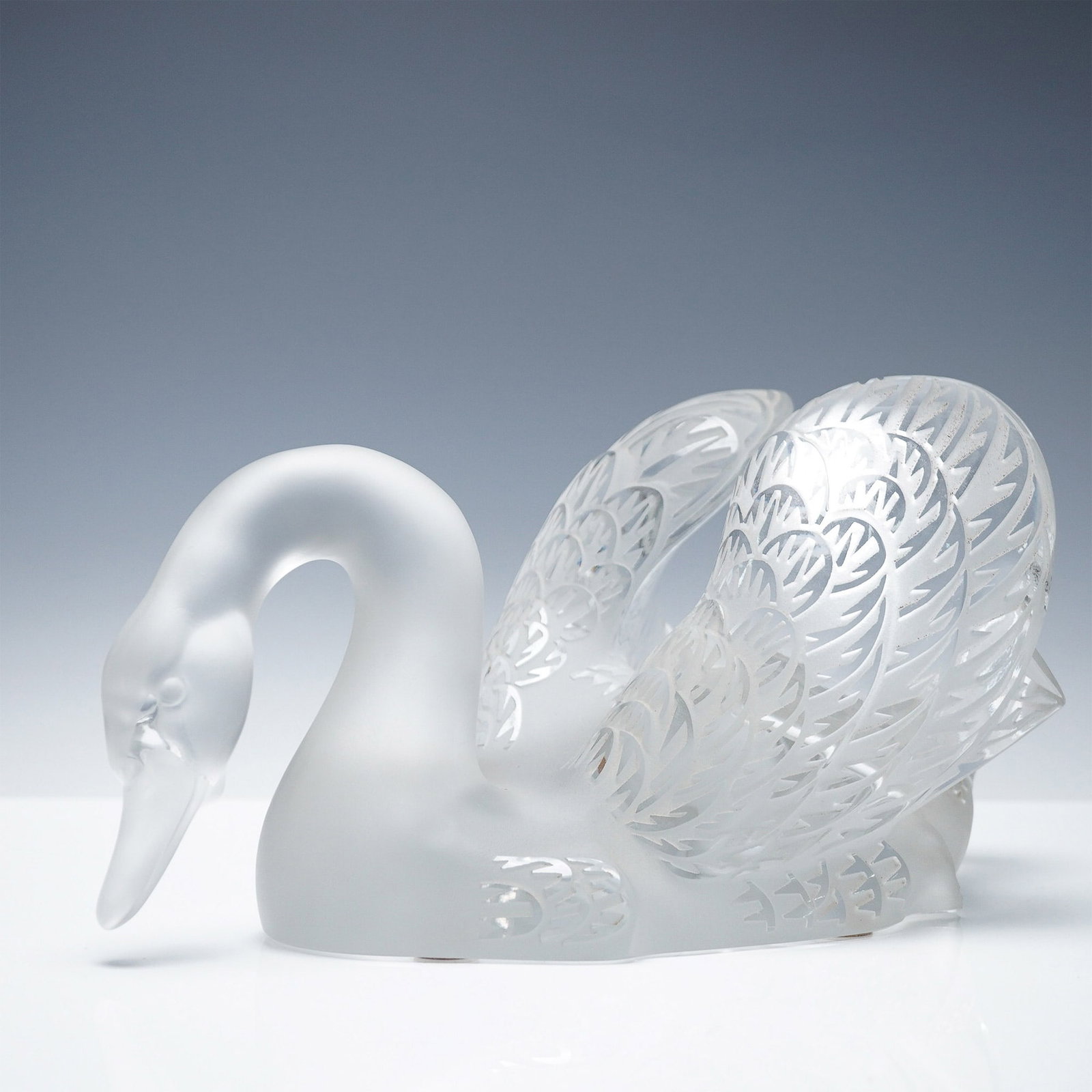 Lalique Crystal Sculpture, Swan - Head Down: Lalique crystal swan sculpture featuring a head-down posture. The figure is crafted from frosted and clear crystal, showcasing intricate feather detailing. The design includes precision-etched plumage