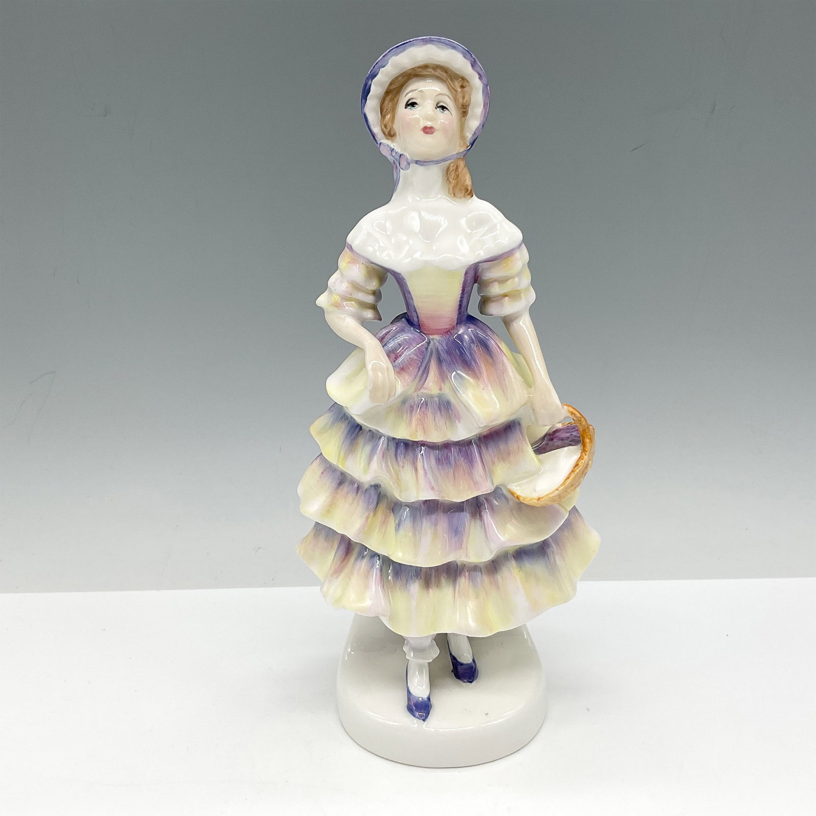 Meg HN2743 - Royal Doulton Figurine: Part of the Classic Pretty Ladies series, figure is dressed in yellow, pink and lavender ruffled dress with a lavender bonnet carrying a basket. Signed and dated by Michael Doulton. Royal Doulton back