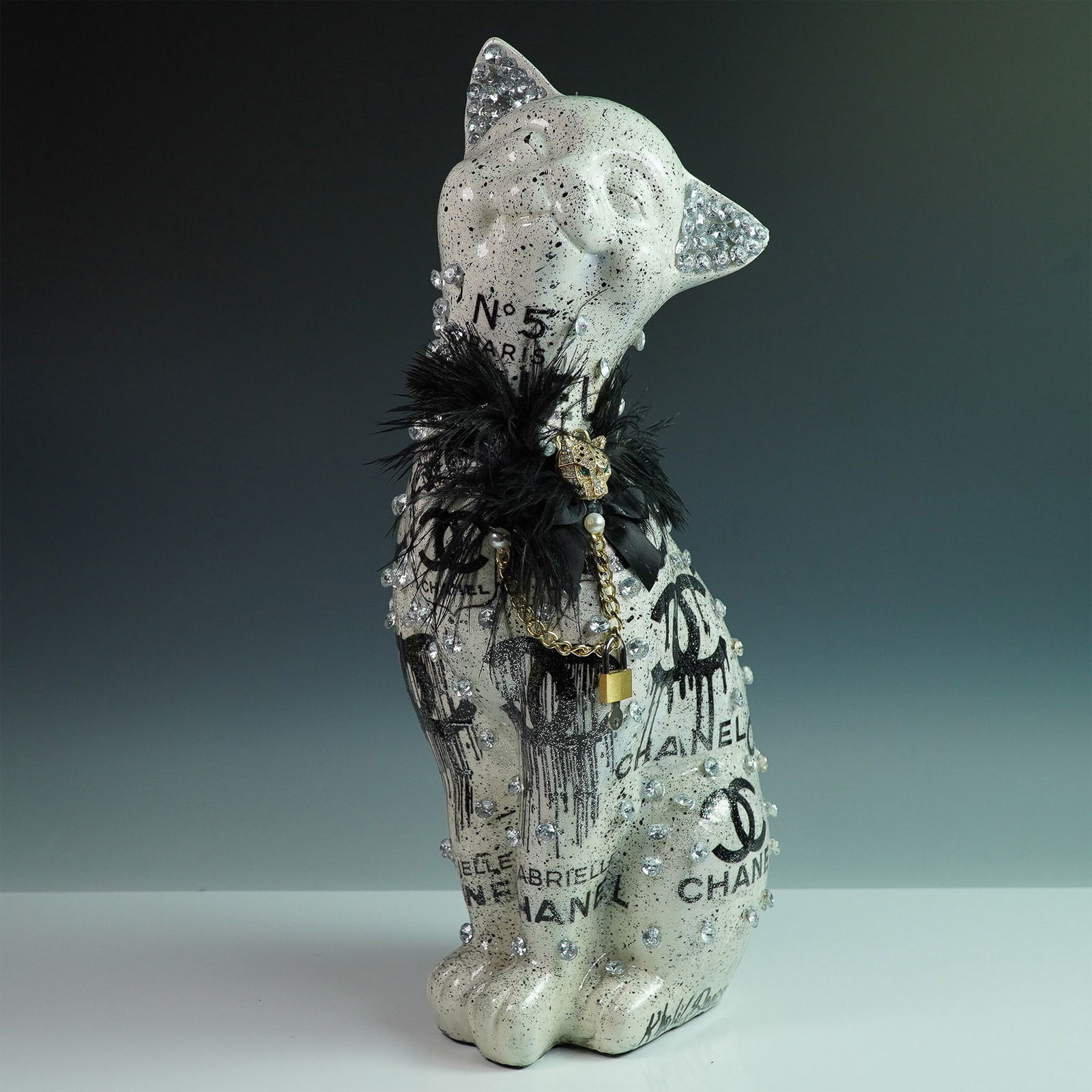 Khalil Douisse Chanel-Inspired Cat Sculpture with Crystal Embellishments: A glamorous mixed-media cat sculpture by Khalil Douisse, featuring an avant-garde Chanel No. 5-inspired design. This striking artwork is finished in a white and black splatter effect, adorned with han