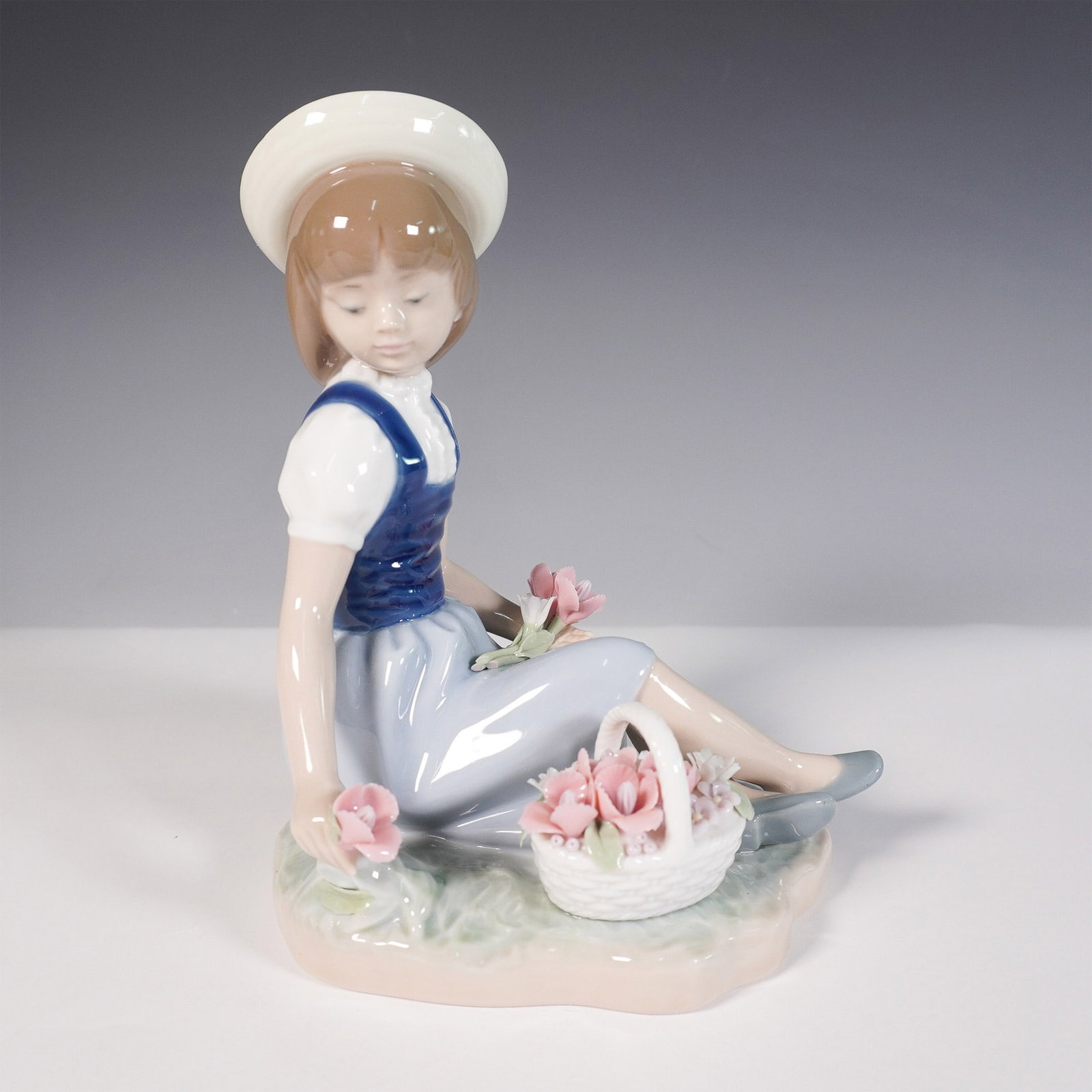 Lladro Porcelain Figurine, Picking Flowers 1001287: Charming hand-crafted porcelain figurine by Lladro, titled Picking Flowers (1001287). Sculpted by Francisco Catala, this serene piece features a young girl in a wide-brimmed hat seated in a meadow, ge