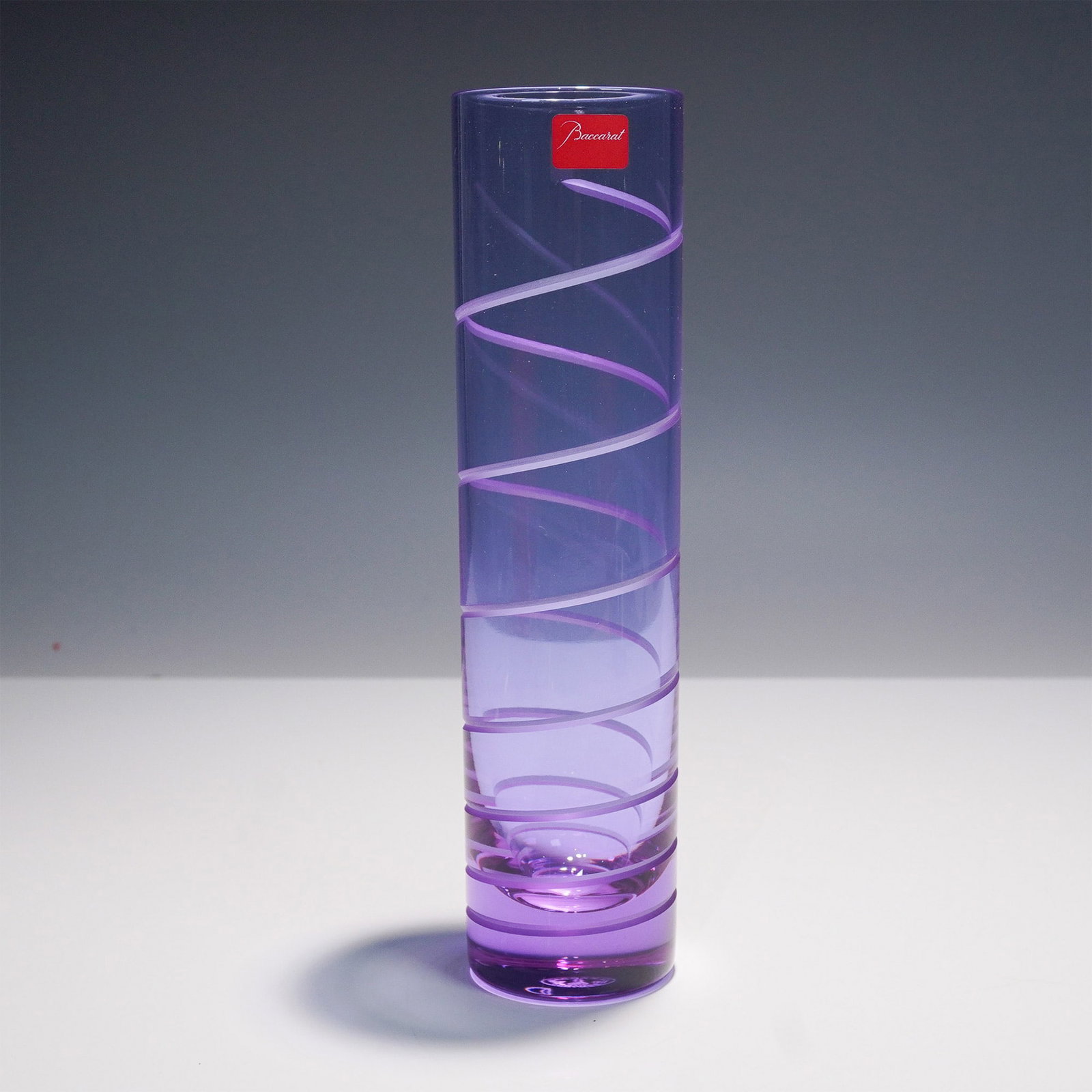Baccarat Crystal Spiral Purple Vase: A striking Baccarat crystal vase from the Spiral collection, featuring a captivating purple hue with a delicate spiral pattern encircling its cylindrical form. The vase showcases Baccarat's renowned c