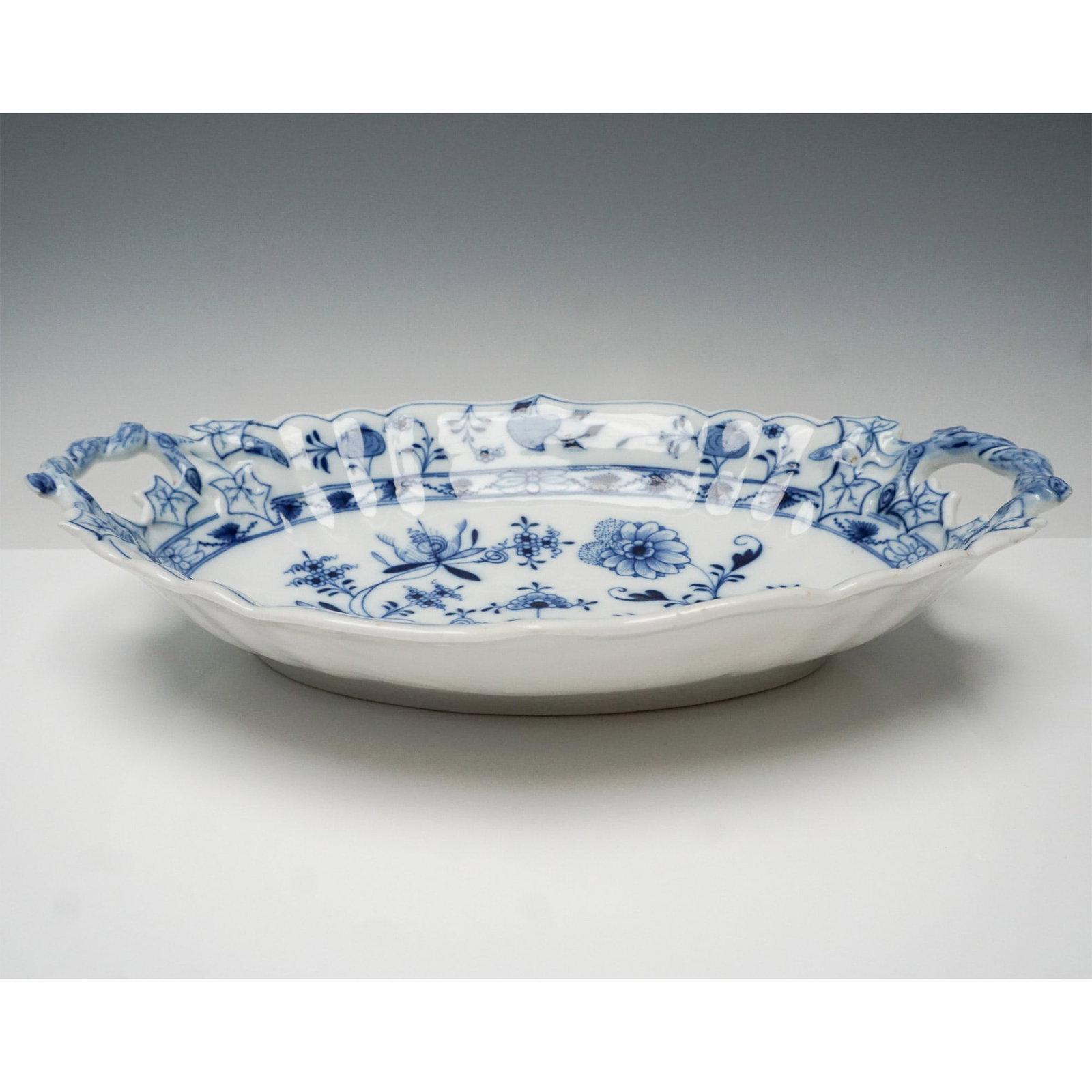 Meissen Blue Onion Handled Porcelain Serving Bowl: This Meissen porcelain serving bowl showcases the iconic Blue Onion pattern, featuring intricate cobalt blue floral and foliate motifs inspired by Chinese porcelain designs. The scalloped rim and orna