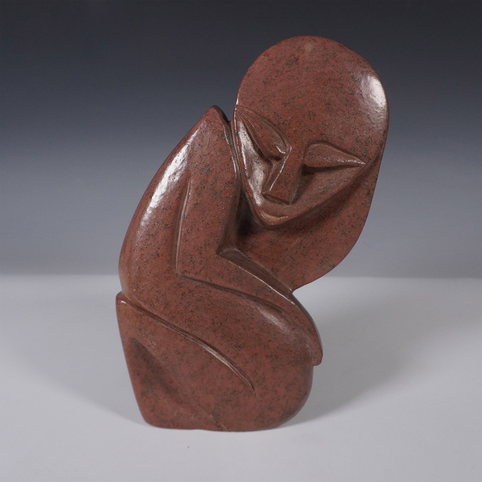 Zimbabwe Shona Stone Sculpture: A hand-carved Shona stone sculpture from Zimbabwe, featuring a modernist abstract form with fluid lines and a contemplative pose. The sculpture is crafted from richly hued stone with a polished finish