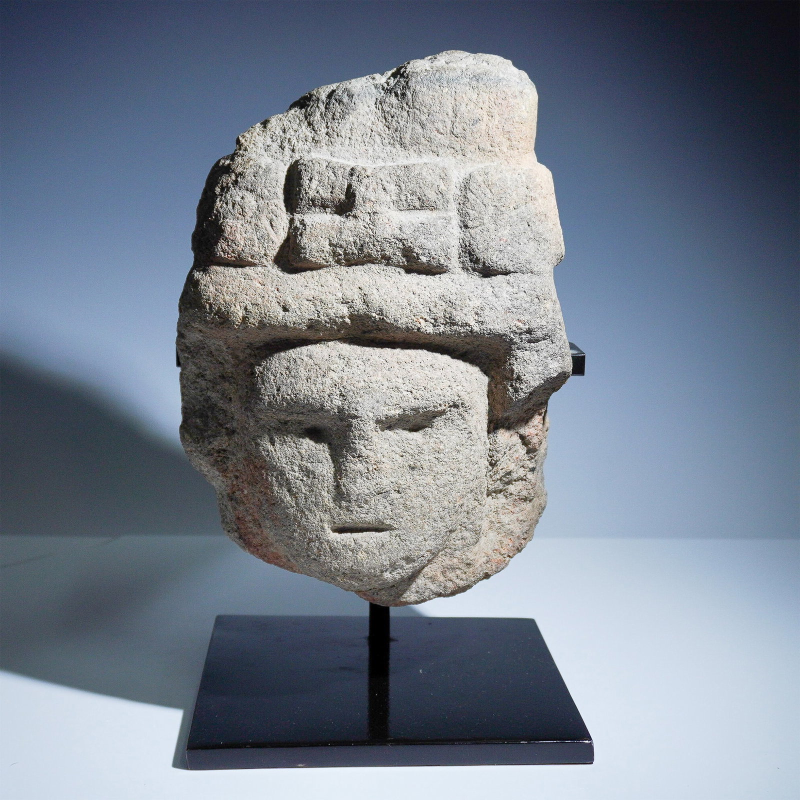 Mesoamerican Carved Stone Head Fragment: A striking Mesoamerican carved stone head fragment, possibly from an ancient civilization such as the Aztecs or Mayans. The piece depicts a stylized human face with deeply incised eyes, nose, and mout