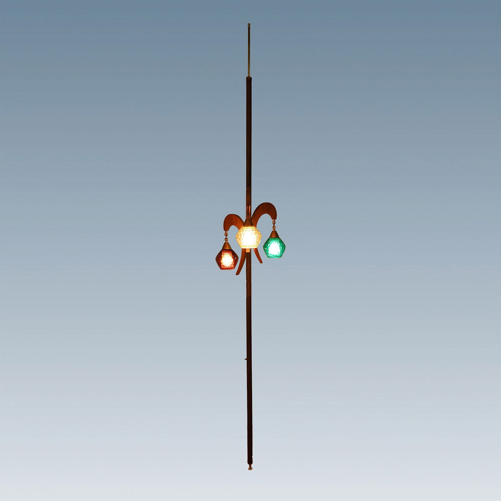 Mid-Century Modern Tension Pole Lamp with Three Glass Shades: This striking mid-century modern tension pole lamp features a sculptural wood and brass frame with three hanging glass shades in amber, emerald green, and deep red. Each textured glass shade emits a w