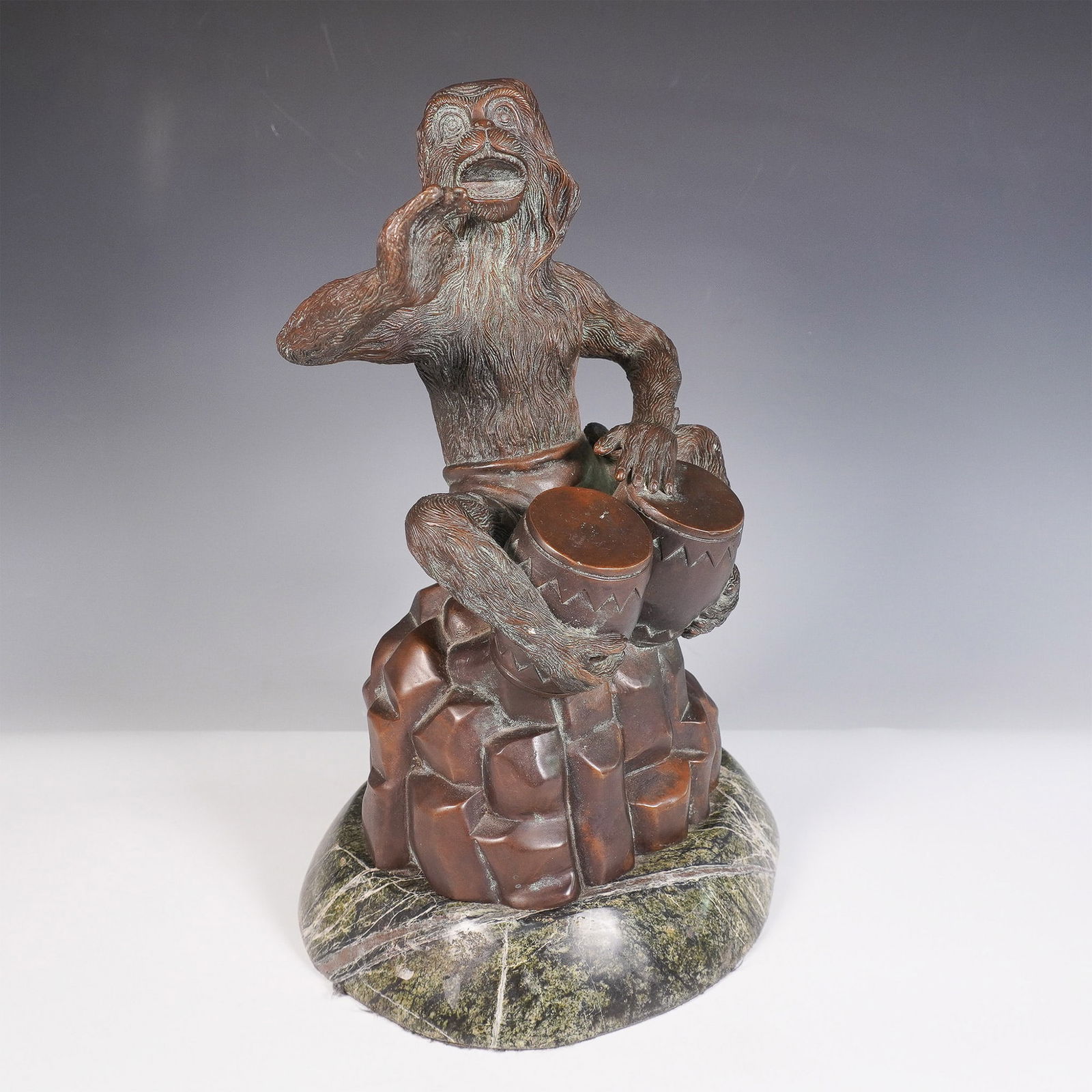Theodore and Alexander Bronze Monkey Bongo Drummer Sculpture: A finely detailed Theodore Alexander bronze sculpture featuring a monkey playing the bongo drums. The figure is seated on a rock-like base, intricately sculpted with lifelike fur texture and expressiv