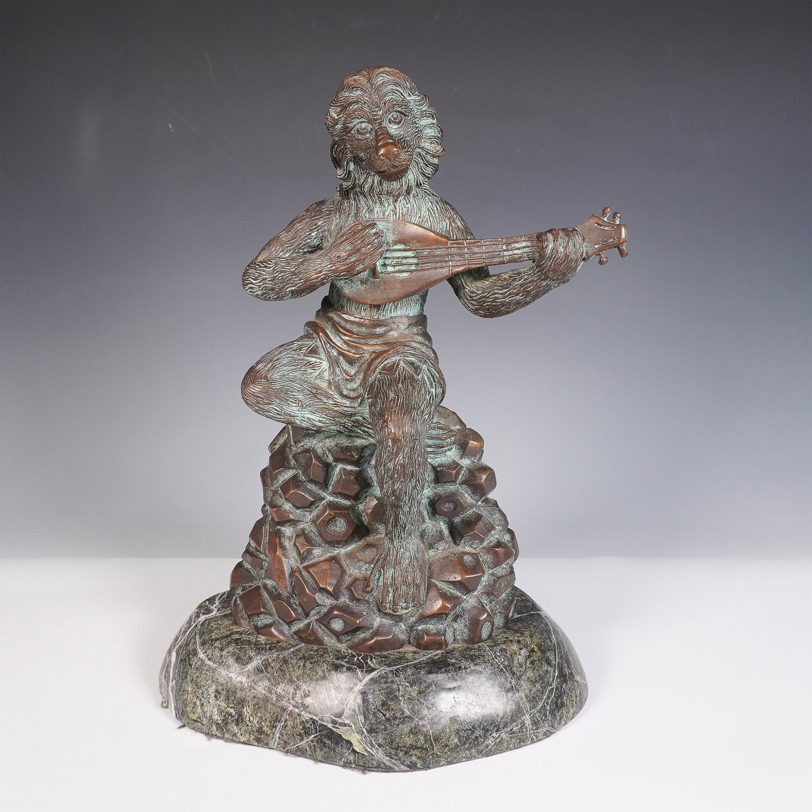 Theodore and Alexander Bronze Monkey Lute Player Sculpture: A finely crafted Theodore Alexander bronze sculpture depicting a monkey playing a lute. The figure is seated atop a rock-textured base, with intricate details in the fur, expressive facial features, a