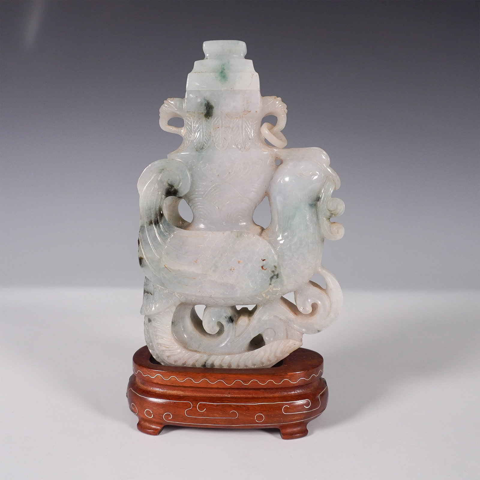 Chinese Carved Jadeite Phoenix and Dragon Vessel with Wooden Stand: A finely carved Chinese jadeite vessel, intricately designed with a phoenix and dragon motif, representing the balance of yin and yang in traditional Chinese culture. This elegant sculpture showcases 