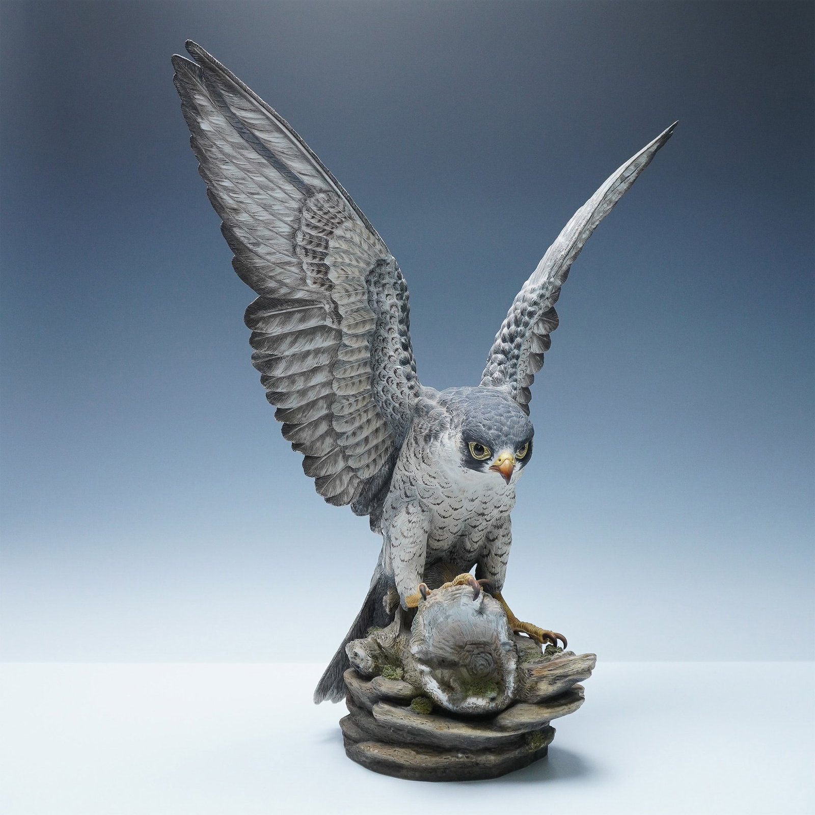 Boehm Limited Edition Peregrine Falcon Porcelain Sculpture: A striking Boehm bone porcelain sculpture depicting a peregrine falcon in mid-hunt, perched atop a rock formation with its talons gripping its prey. The falcon's wings are fully extended, showcasing i