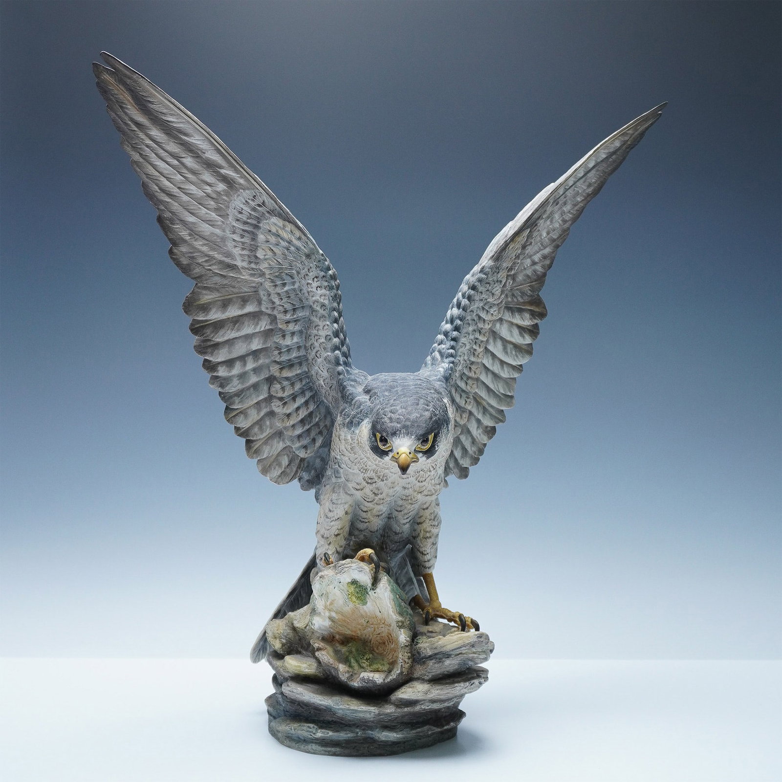 Boehm Limited Edition Peregrine Falcon Porcelain Sculpture: A striking Boehm bone porcelain sculpture depicting a peregrine falcon in mid-hunt, perched atop a rock formation with its talons gripping its prey. The falcon's wings are fully extended, showcasing i