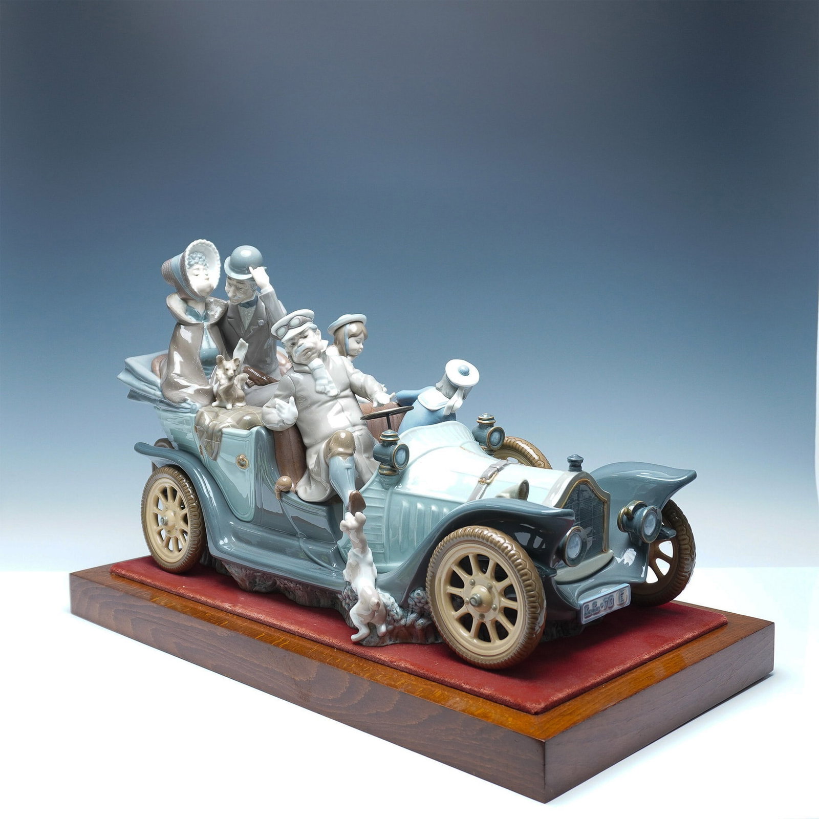 Lladro Porcelain Antique Car on Wood Base 01001146: A whimsical Lladro porcelain sculpture titled Antique Car, capturing the charm of a vintage automobile ride with a family enjoying their journey. The intricate detailing brings this delightful scene t