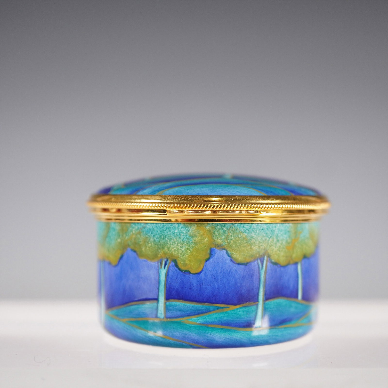 Moorcroft Oval Enamel Pot in Moonlit Blue: A Moorcroft oval enamel pot in the sought-after Moonlit Blue design, featuring a tranquil landscape of rolling hills and trees bathed in deep blues and greens. This beautifully hand-painted enamel pie