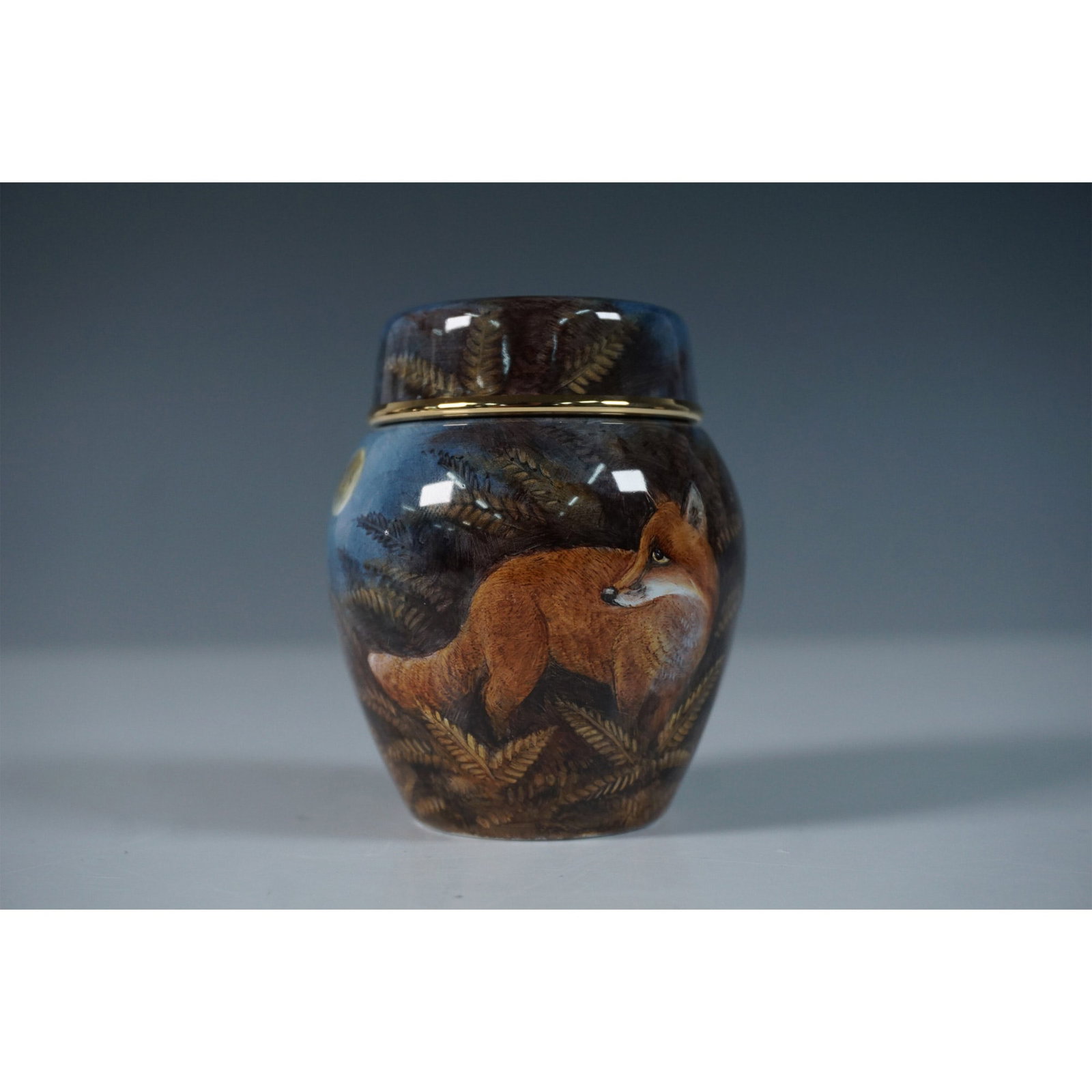 Moorcroft Enamel by Terry Halloran Ginger Jar, The Fox: Designed by Terry Halloran, this Moorcroft enamel ginger jar is a beautifully crafted miniature piece featuring a rounded, bulbous body that tapers slightly towards the base. The removable domed lid i