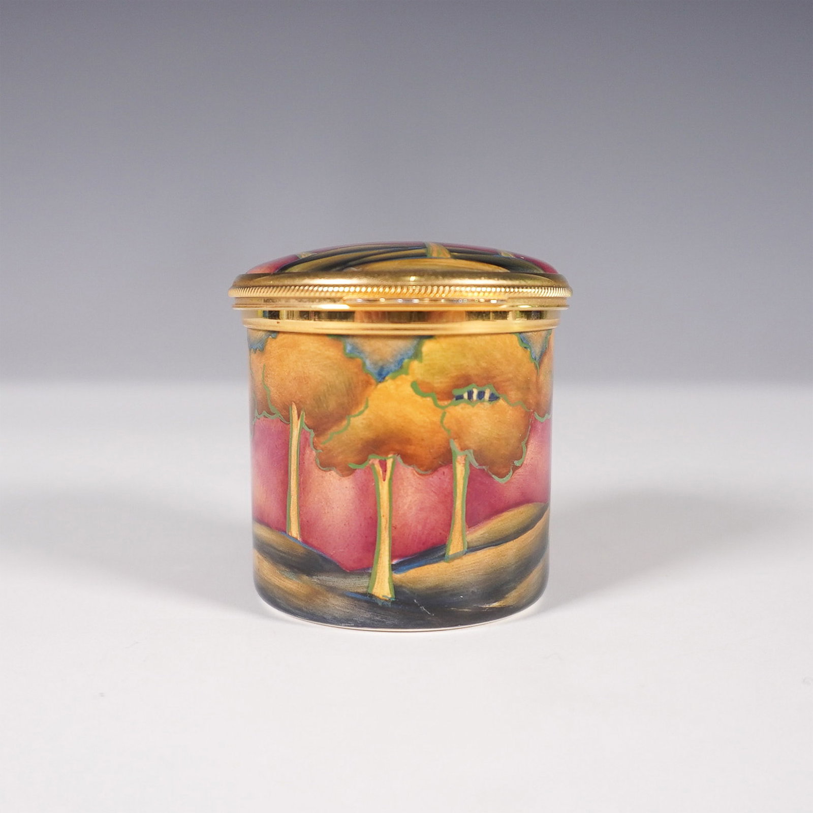 Moorcroft Enamel Box - Golden Trees Design: A Moorcroft enamel box featuring a beautifully hand-painted landscape of golden trees set against a rich pink gradient background. The hinged lid, adorned with gold trim, opens to reveal an interior i