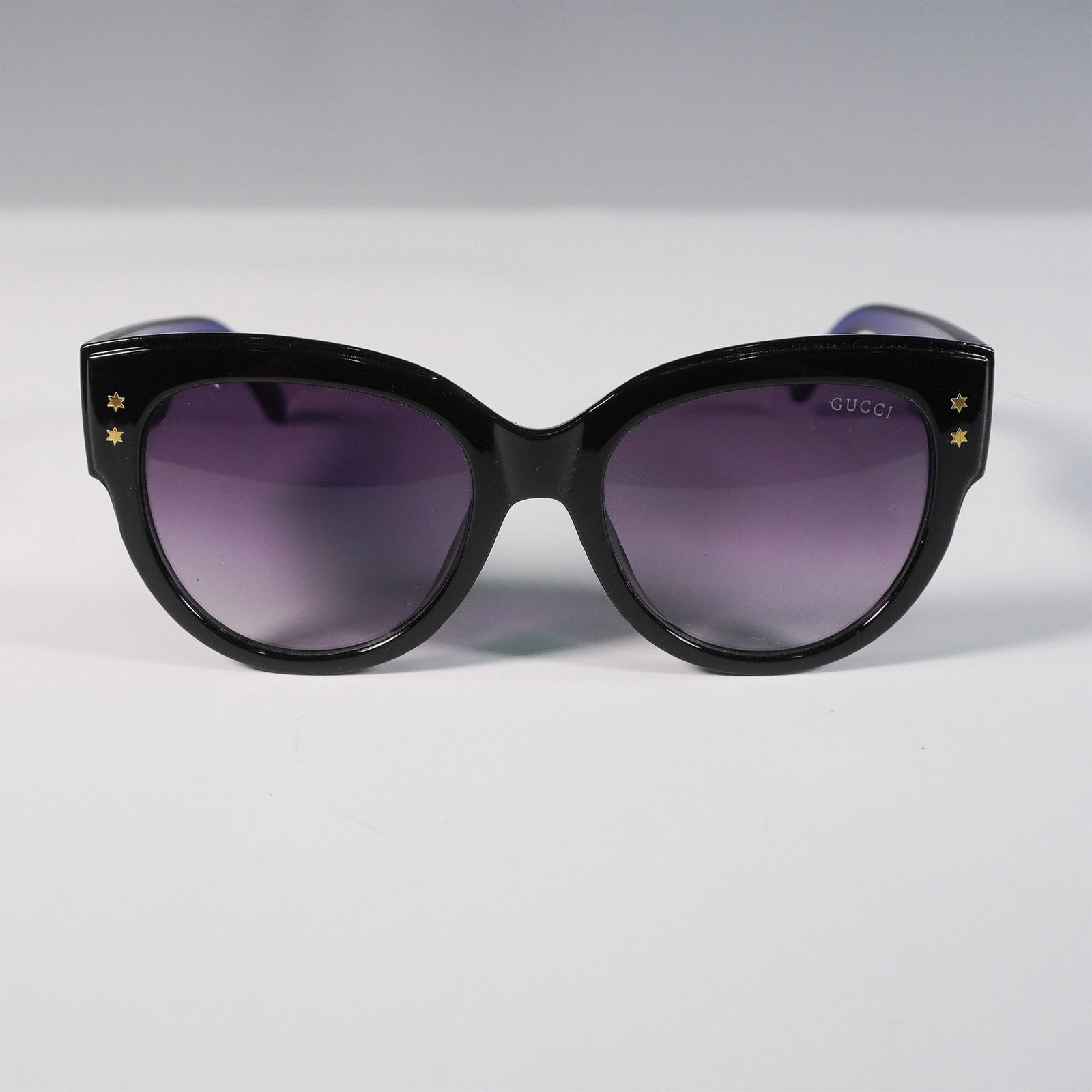 Sunglasses in the Style of Gucci, GG3864 Design: Fashion-forward sunglasses inspired by the bold styling of Gucci, featuring a black frame with translucent blue arms and red stripe detail. The design includes gold-tone interlocking GG-style emblems